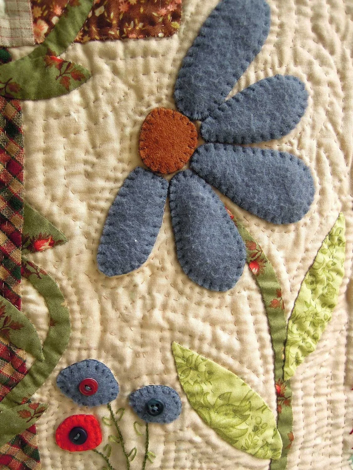 Close-up of a quilt with blue and red felt flowers and green leaves on a cream background.