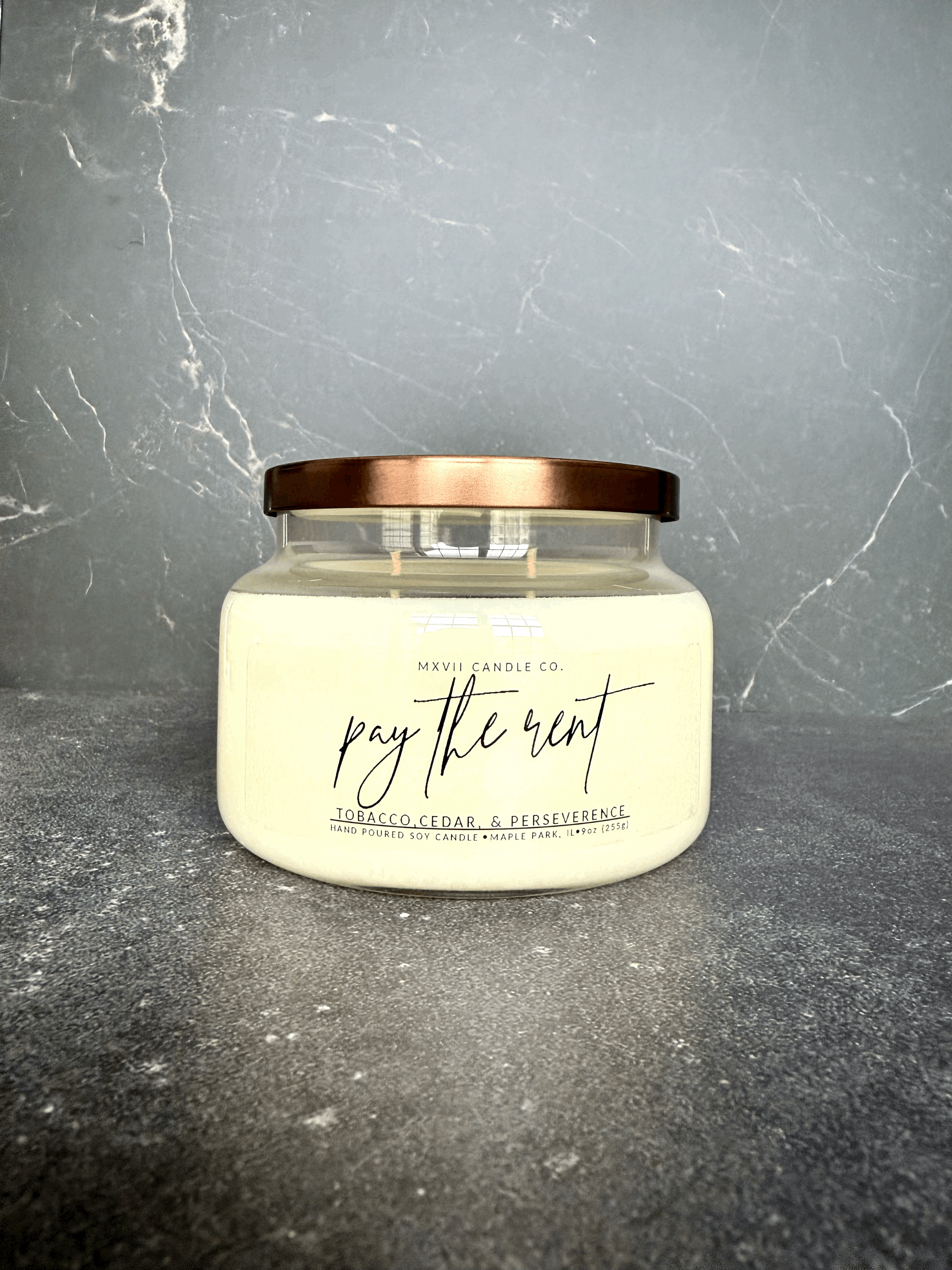 Tobacco Cedar soy candle in a clear jar with copper lid on black marble background — Pay the Rent by MXVII Candle Co.