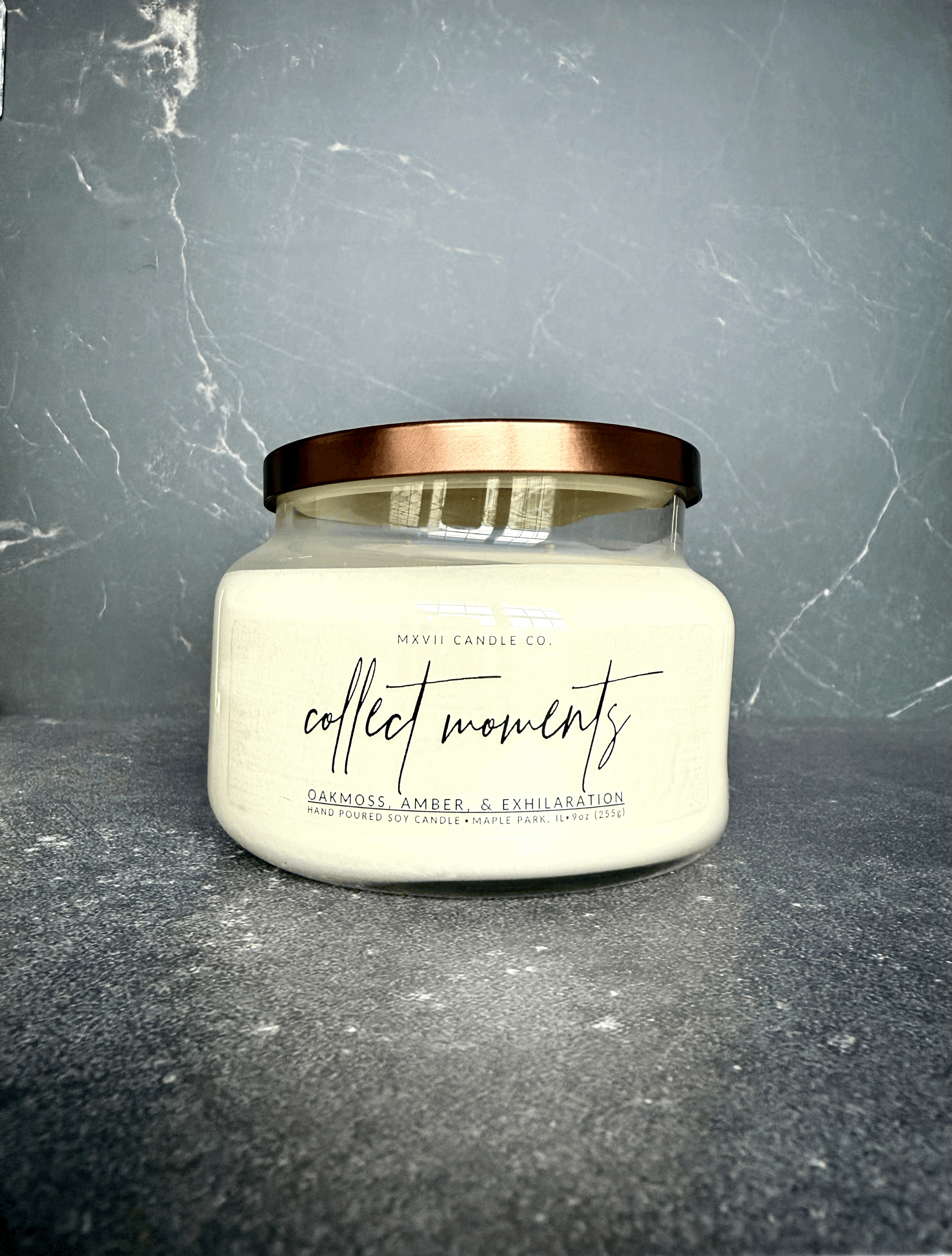 Oakmoss Amber soy candle in a clear jar with copper lid on black marble background — Collect Moments by MXVII Candle Co.