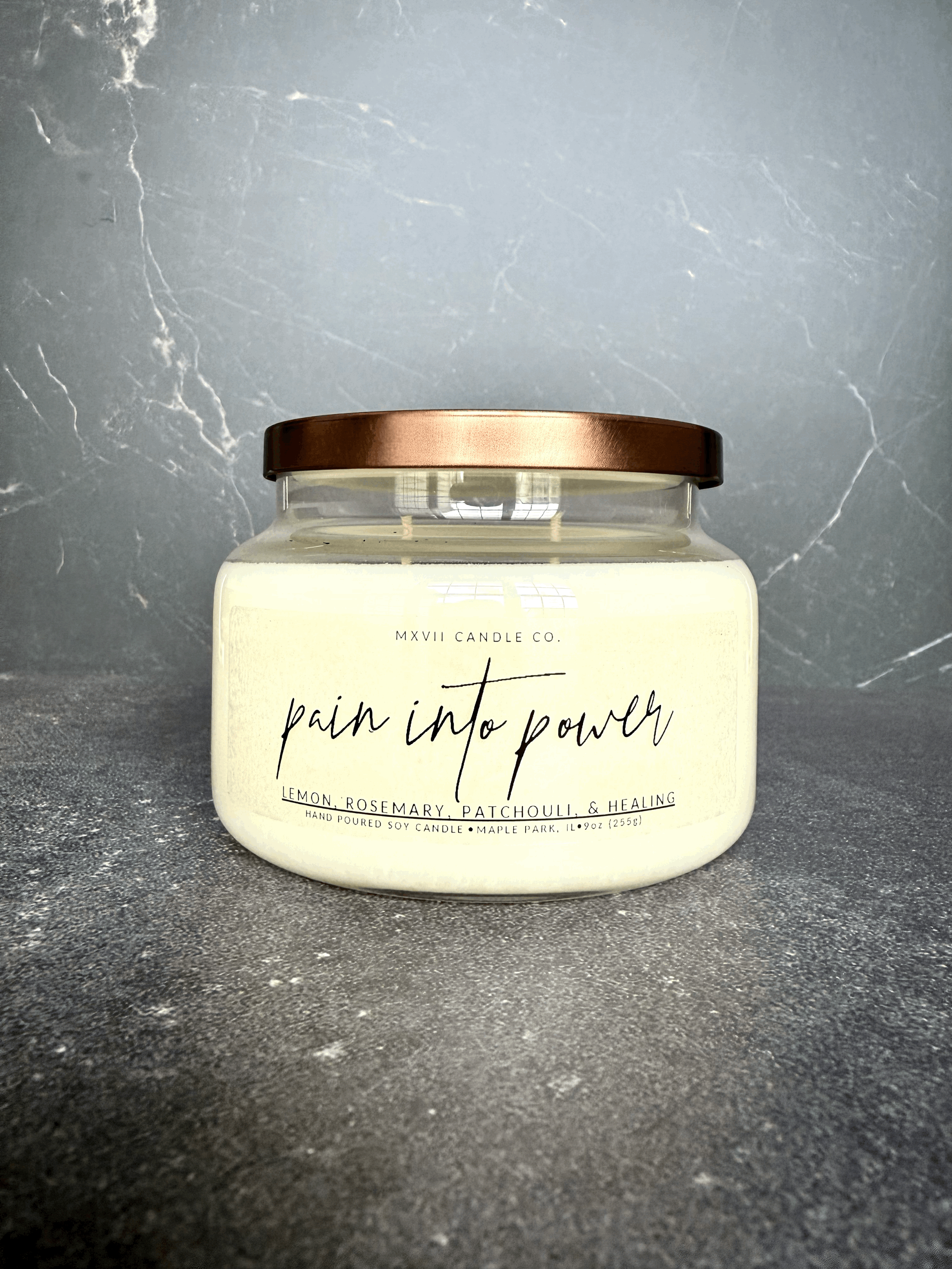 Lemon Rosemary Patchouli soy candle in a clear jar with copper lid on black marble background — Pain into Power by MXVII Candle Co.