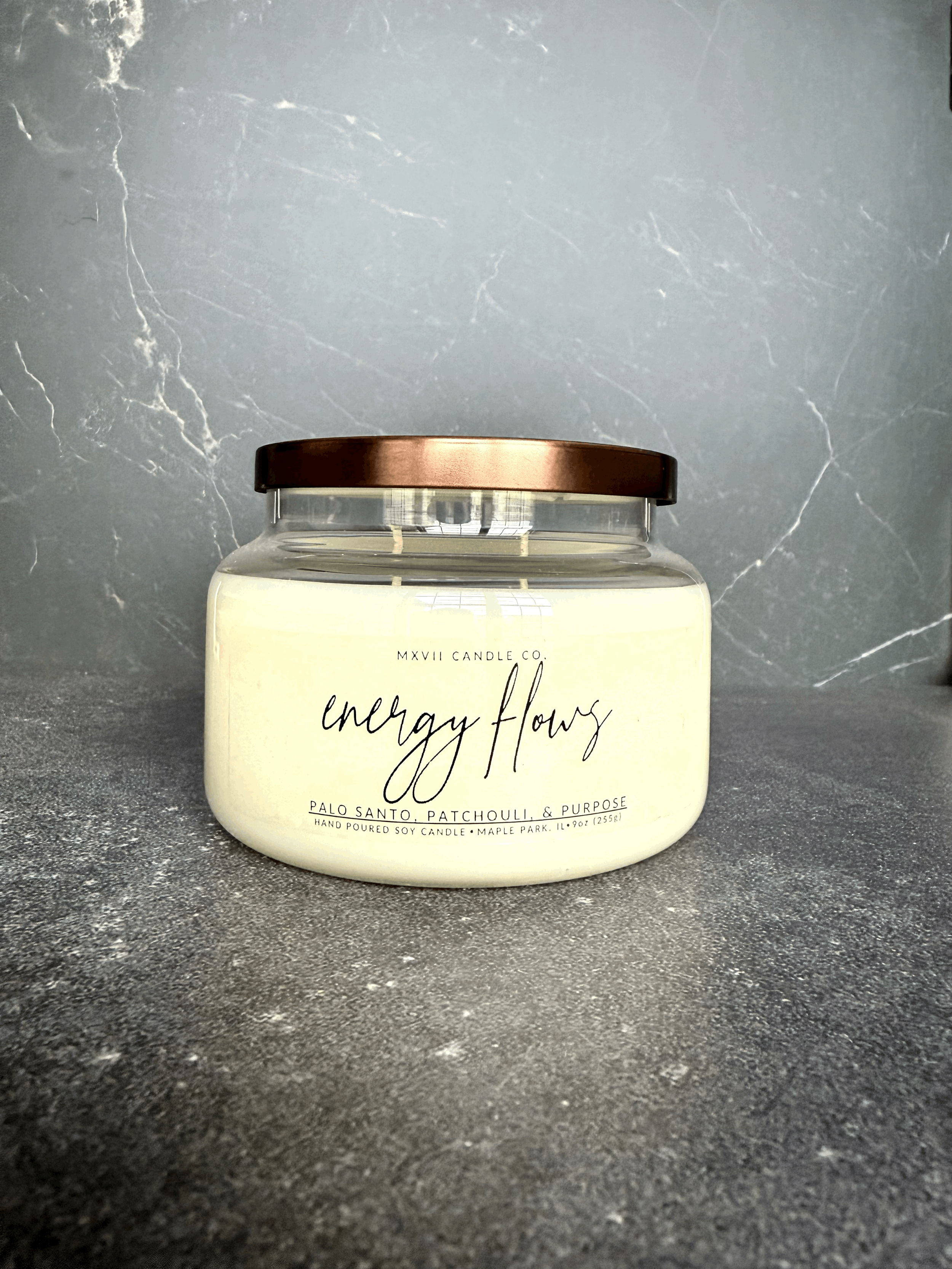 Palo Santo Patchouli soy candle in a clear jar with copper lid on black marble background — Energy Flows by MXVII Candle Co.