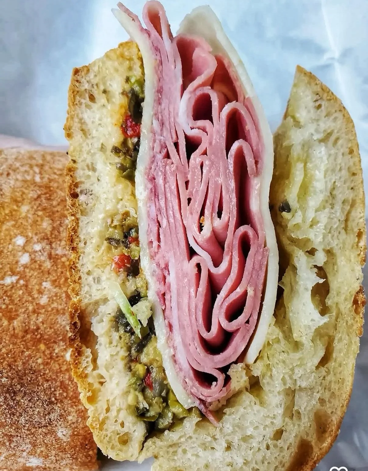 Close-up of a bread roll filled with sliced ham, cheese, and chopped green and red peppers.