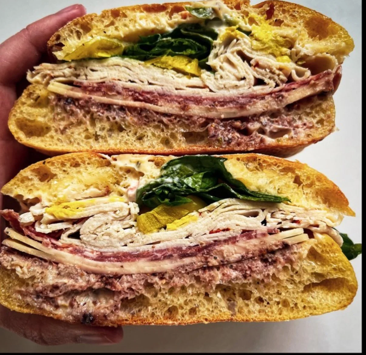 Cross-section of a stuffed bread sandwich with turkey, ham, spinach, pickles, and cheese.