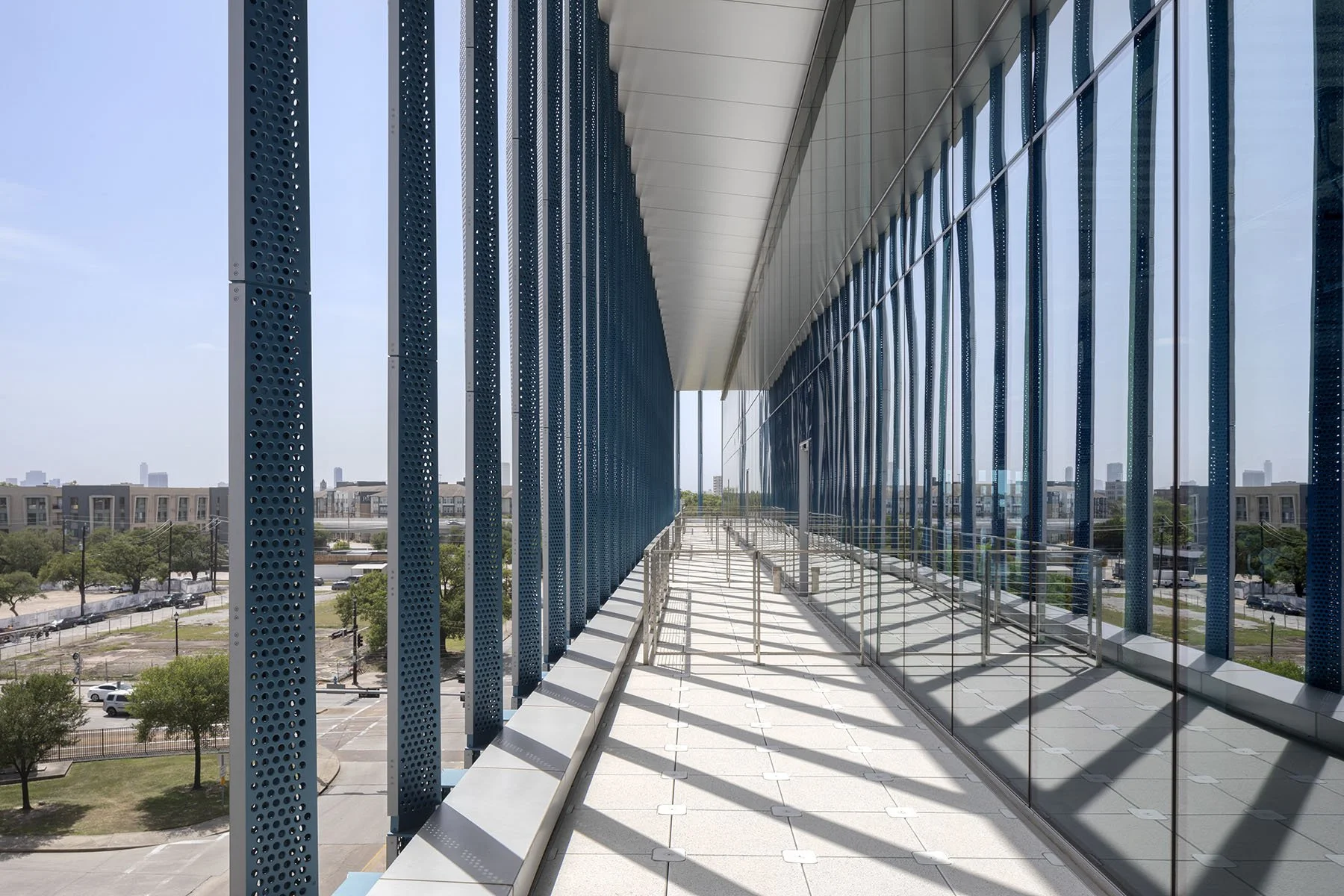 Protected outdoor balcony space on 4th floor with glass on right and view of landscape on left 