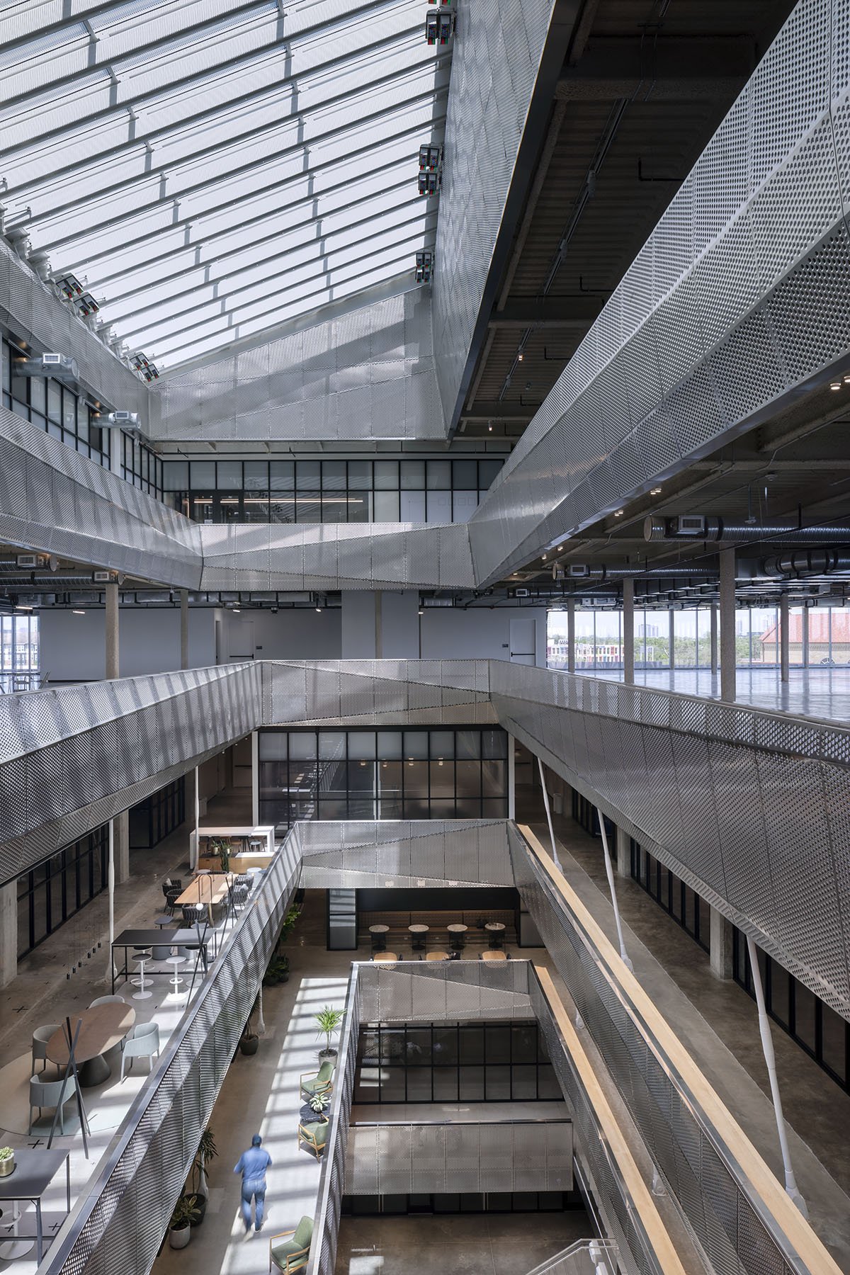 Multi-storey interior atrium with perforated metal balconies, open workspaces, and seating areas on each floor.