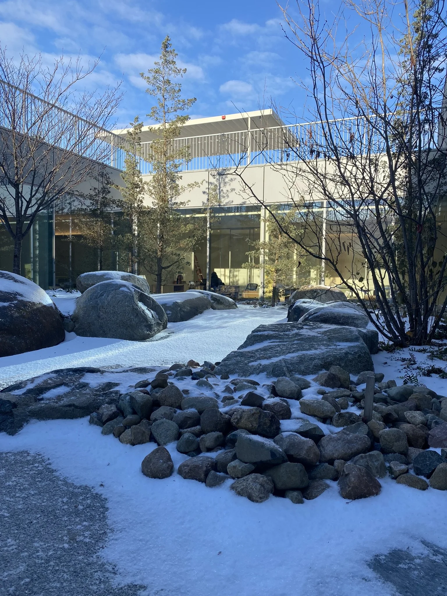 Snow-covered rock garden courtyard outside a modern glass building on a clear winter day.