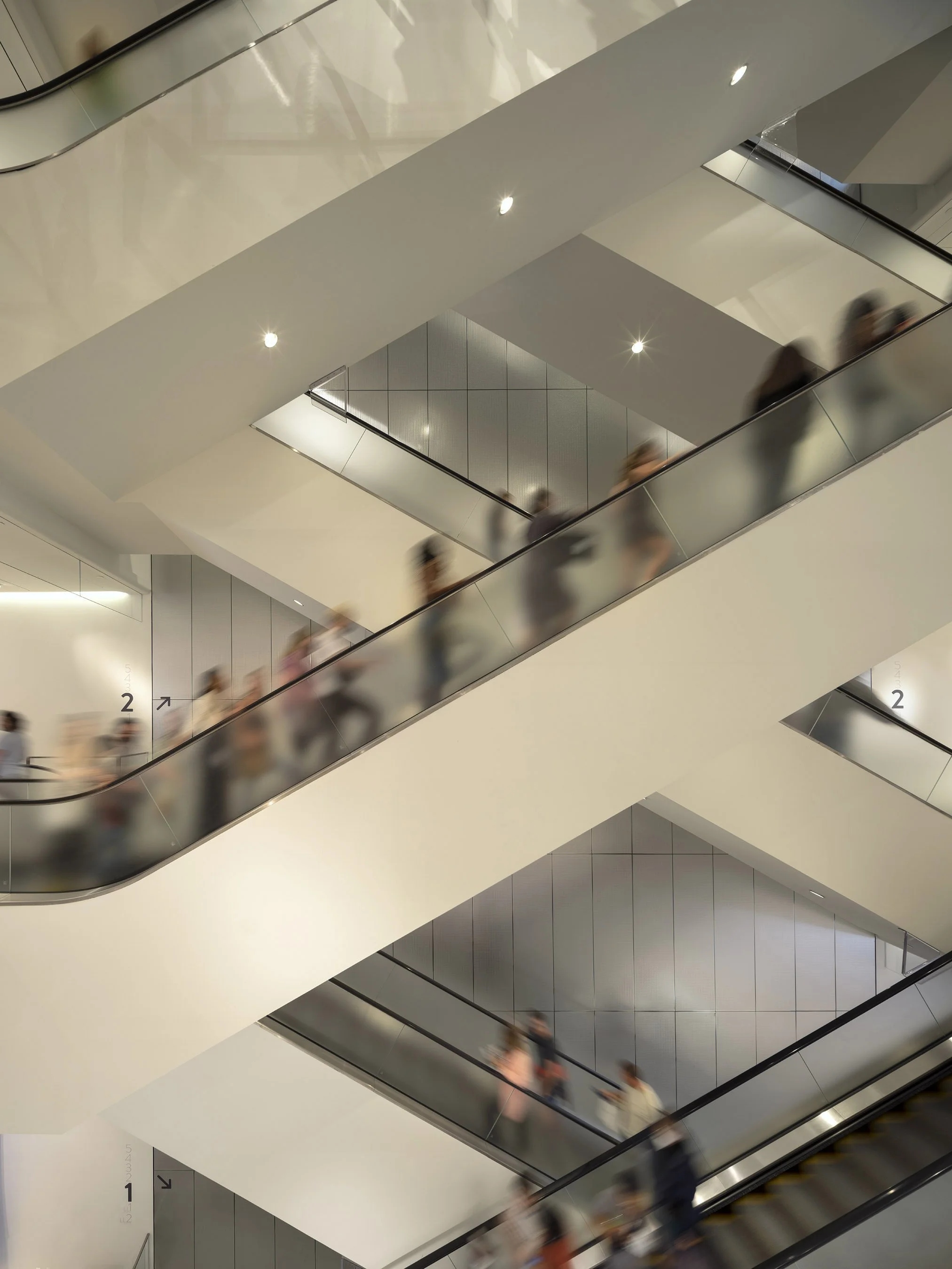 light and flow of people vertically, diffuse glass on escalators that softens the space