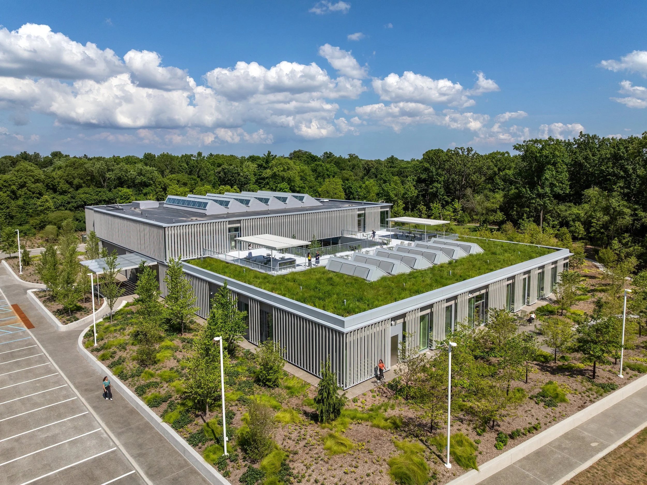 drone shot of full building with grass roof and surrounding landscaping against blue sky