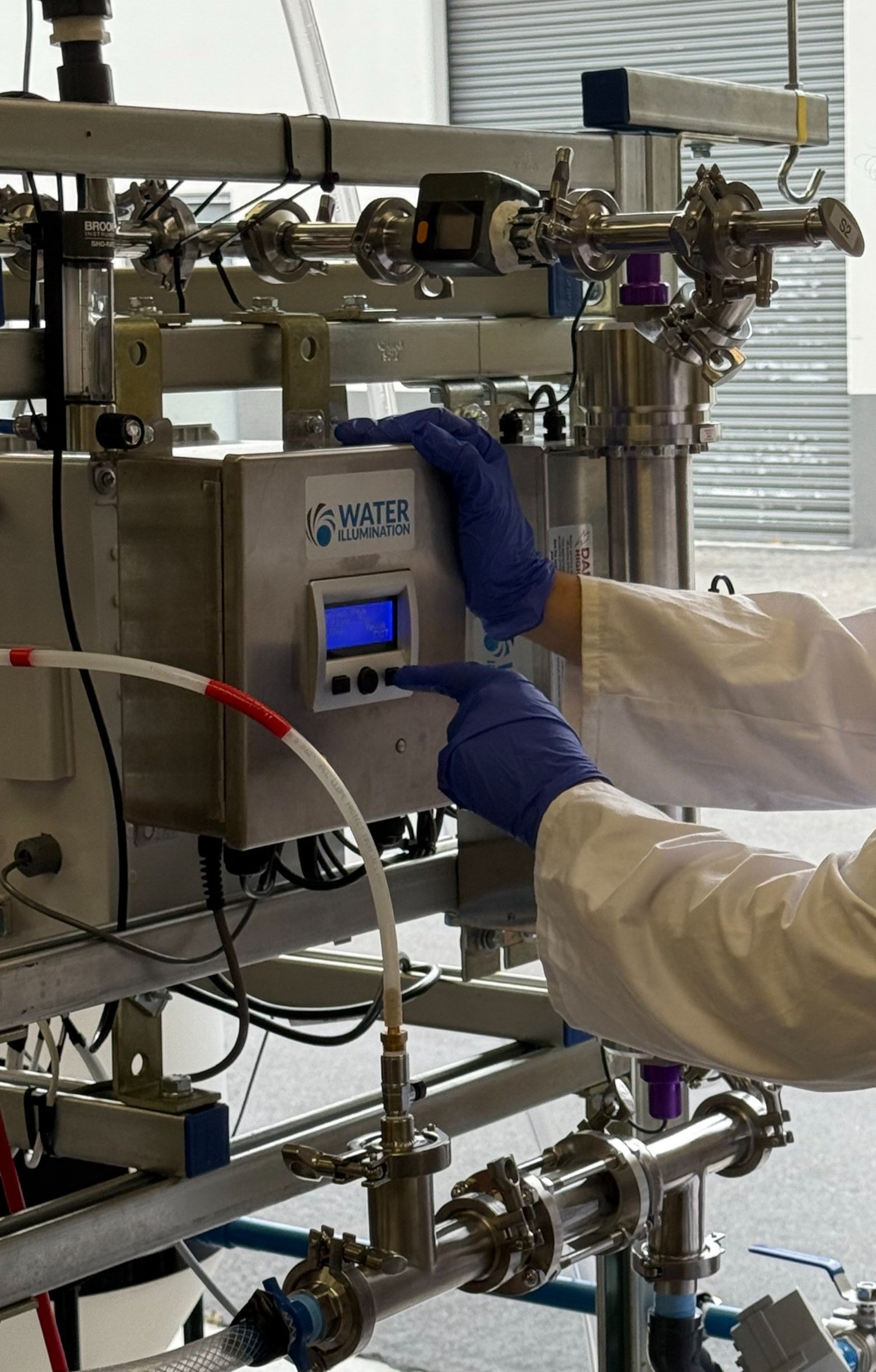 A person in a white lab coat with blue gloves operating a water illumination machine in a laboratory setting.