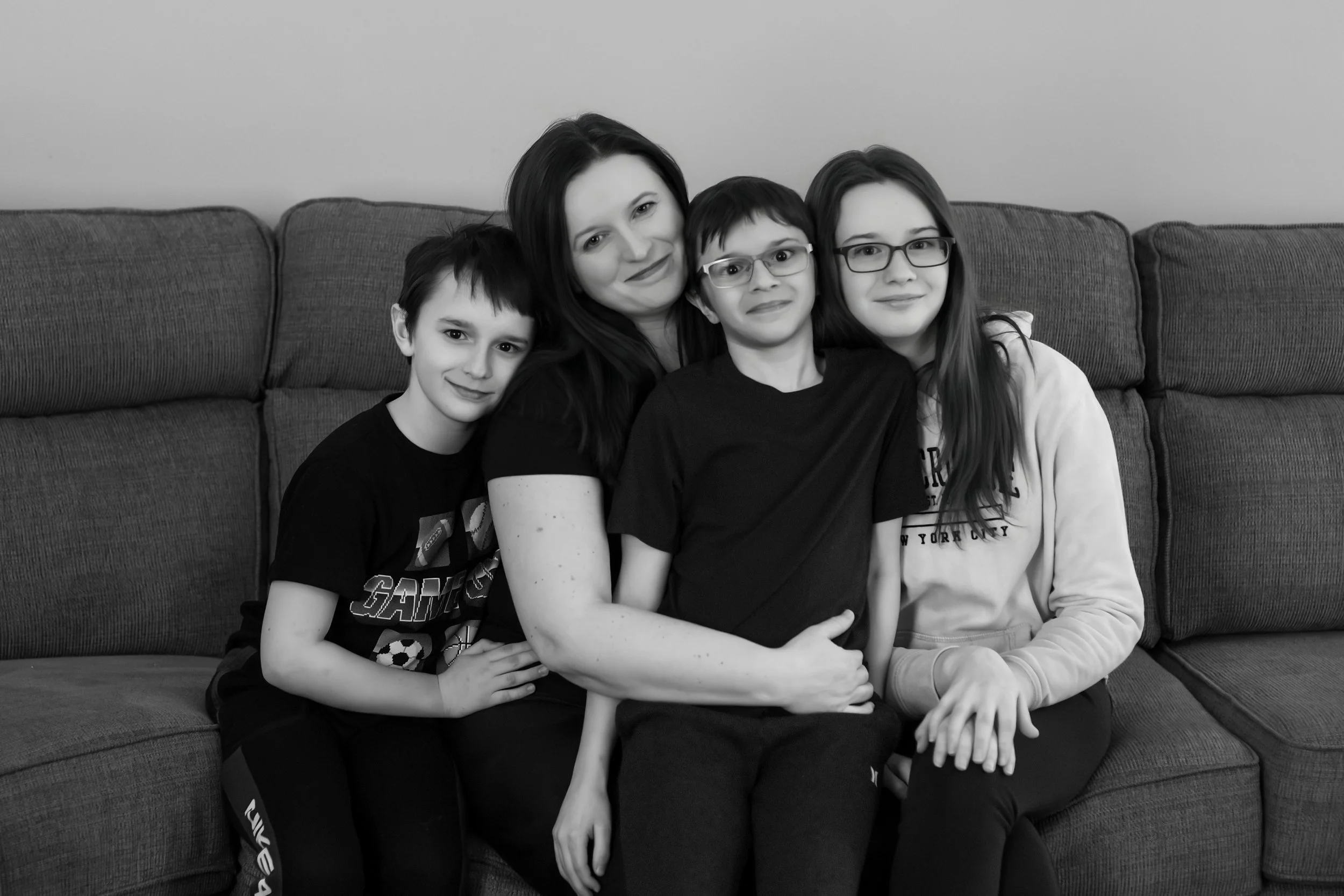 A woman with three children sitting on a sofa, smiling for a black and white photo.