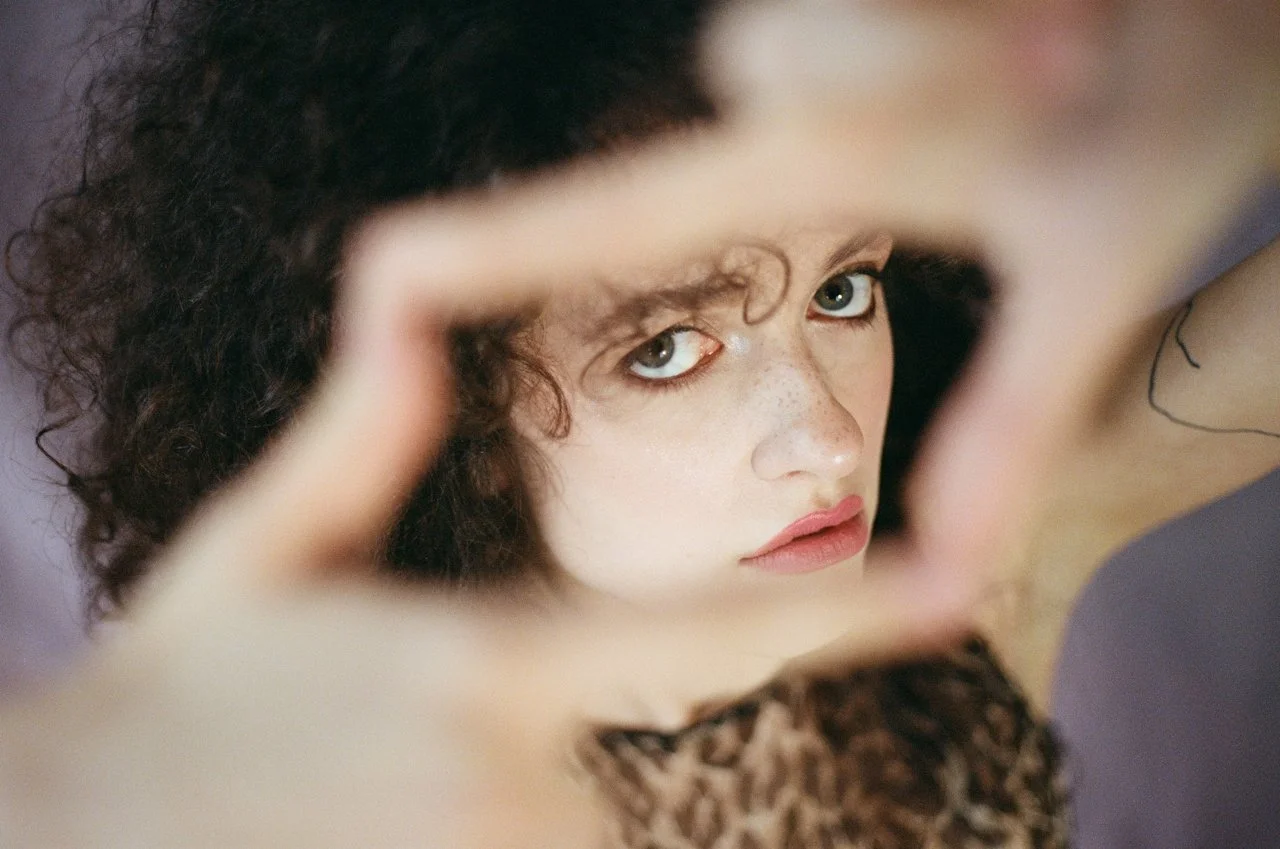 Person with curly hair and freckles looking through hands forming a rectangle