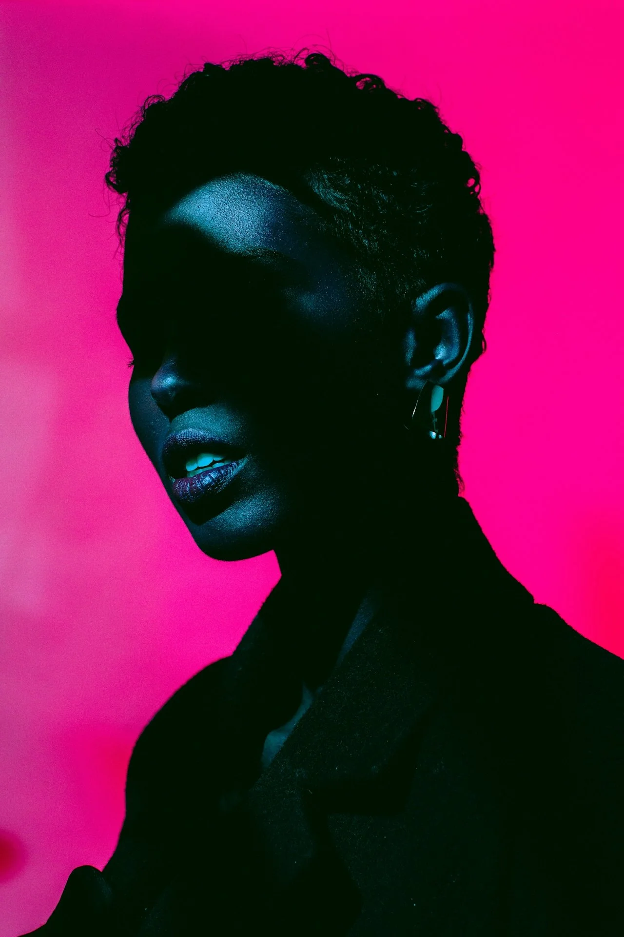 Silhouette of a person against a bright pink background with dramatic shadow over face.