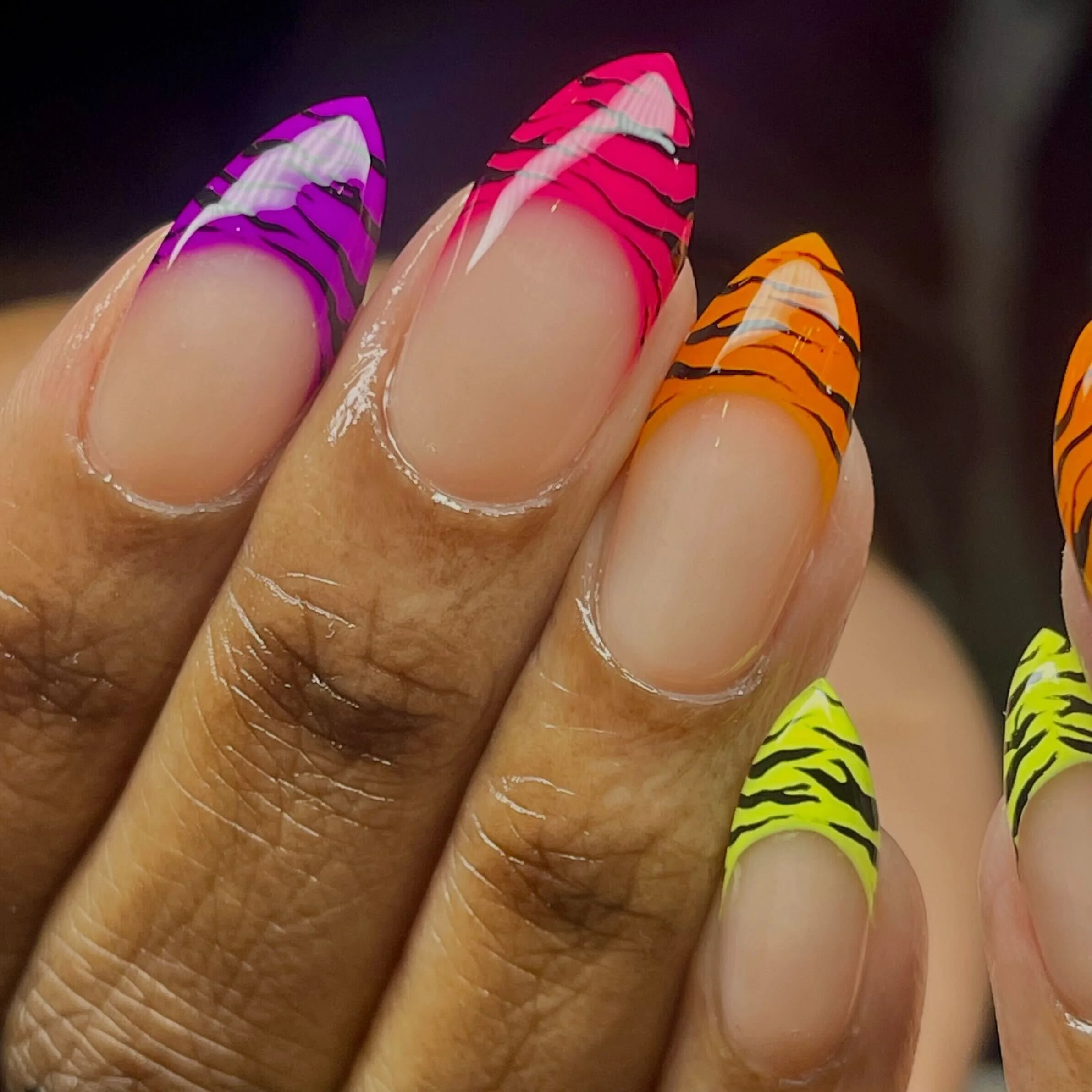Close-up of fingernails with tiger stripe patterns in purple, pink, orange, and yellow colors.