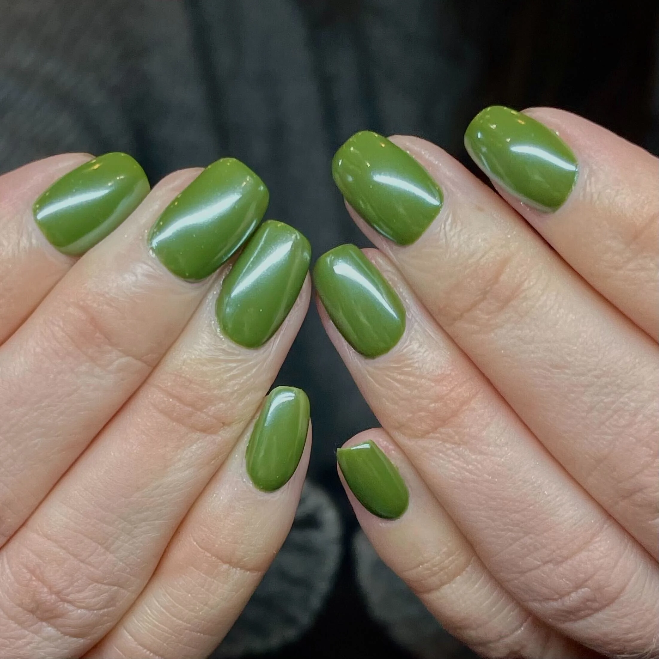 Close-up of hands with freshly manicured nails painted in glossy green polish.