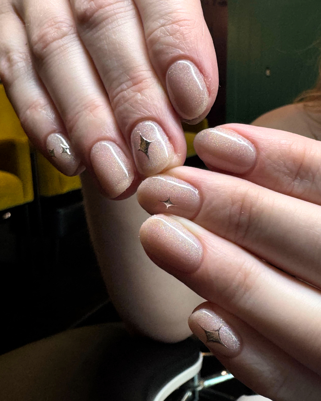 Close-up of hands with manicured nails painted in shimmery nude color with small star-shaped decorations.
