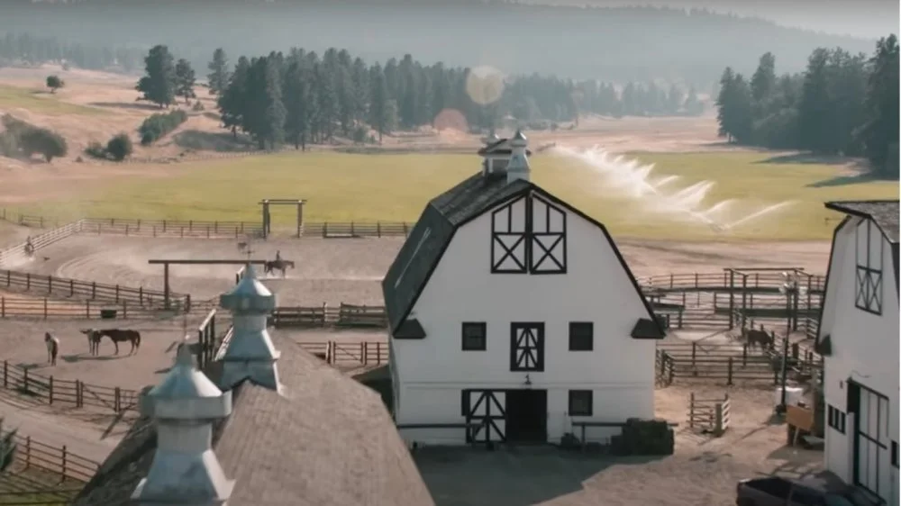 Aerial view of a rural farm with white barns, fenced areas for horses, and green fields with irrigation systems.