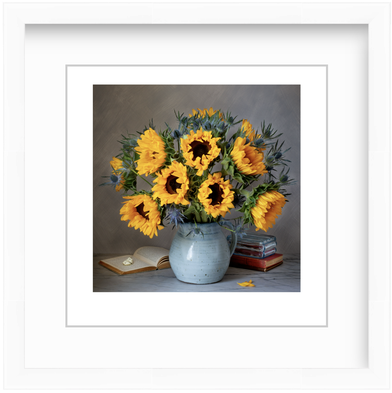 Sunflowers arranged with vintage books and a butterfly in a moody studio still life, lit with soft, dramatic lighting against a dark background.