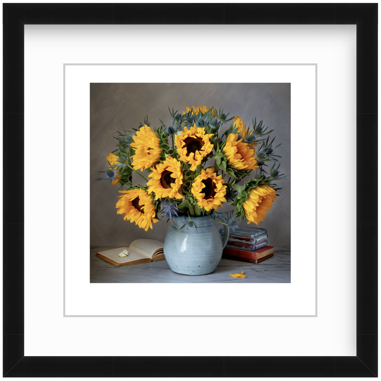 Sunflowers arranged with vintage books and a butterfly in a moody studio still life, lit with soft, dramatic lighting against a dark background.