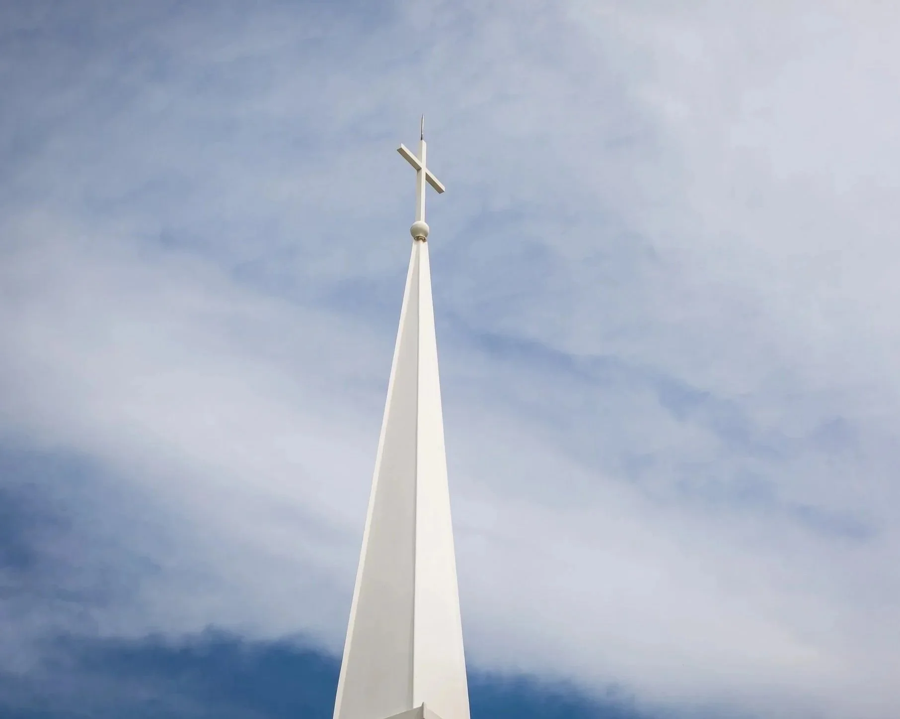 White church steeple with a cross on top against a blue sky with light clouds.