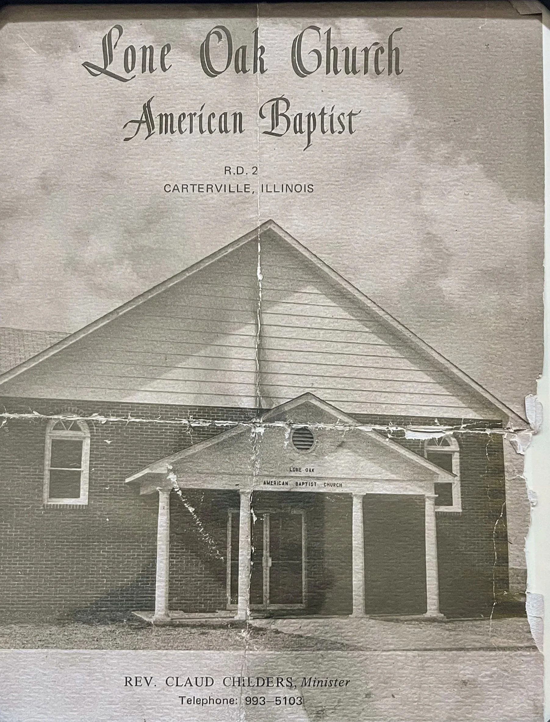 A black and white photo of the front of a church building with a gabled roof and columned entrance. The sign above the entrance reads 'Lone Oak American Baptist' and a smaller sign underneath displays the address 'Lone Oak, American Baptist Church.'