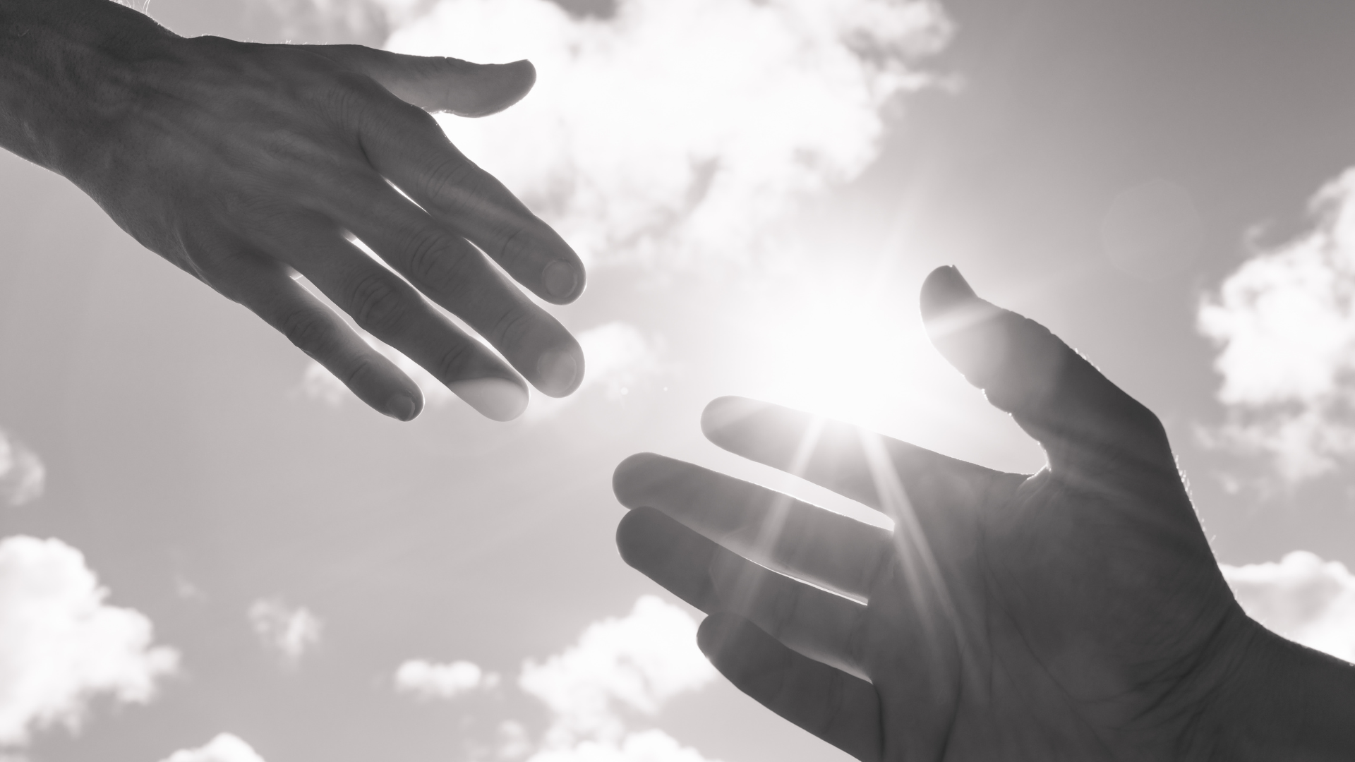 Two hands reaching towards each other against a sky with clouds and sunlight.