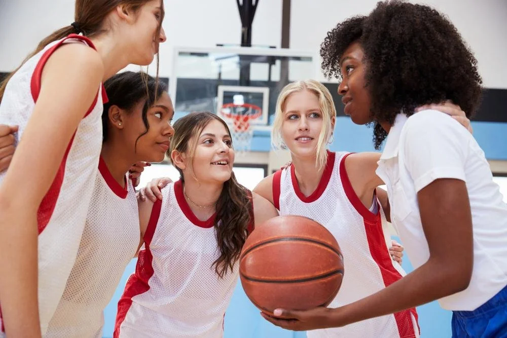 Girls' basketball team huddled together on court with coach giving them a pep talk.