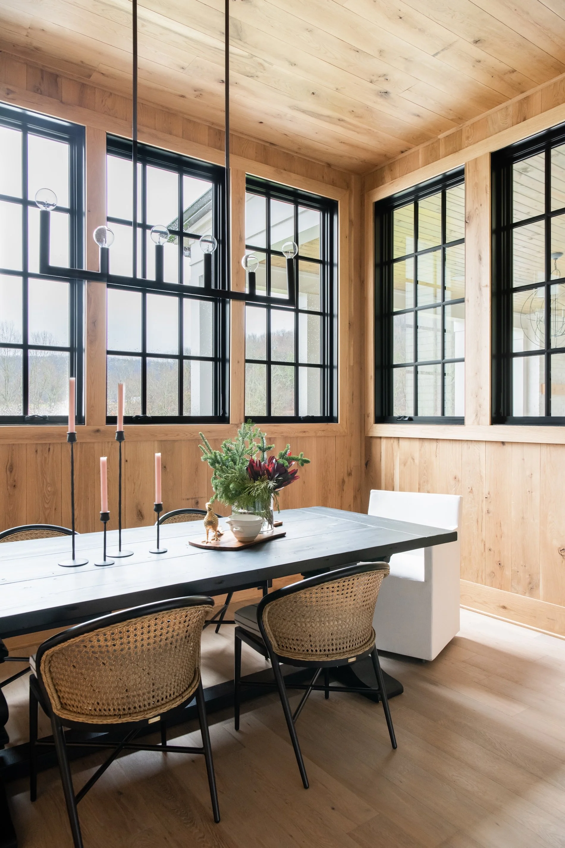 A wooden table in front of custom windows, with a chandelier above
