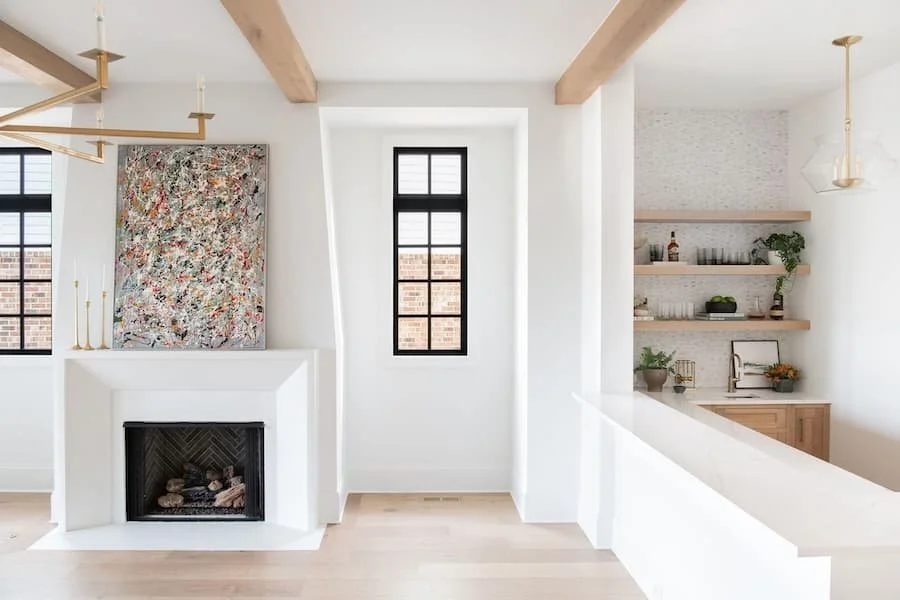 fireplace mantels / fireplace mantel ideas - minimalist white fireplace with exposed beams on ceiling and colorful art on the mantel