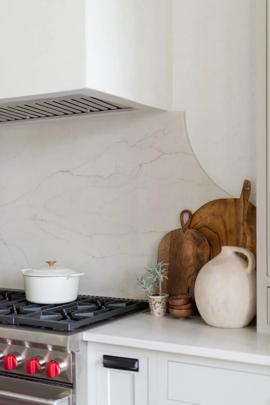 chefs kitchen - picture of styled countertop next to a stove. the stove has a white enameled cast iron Dutch oven on it and the counter has cutting boards and a large urn