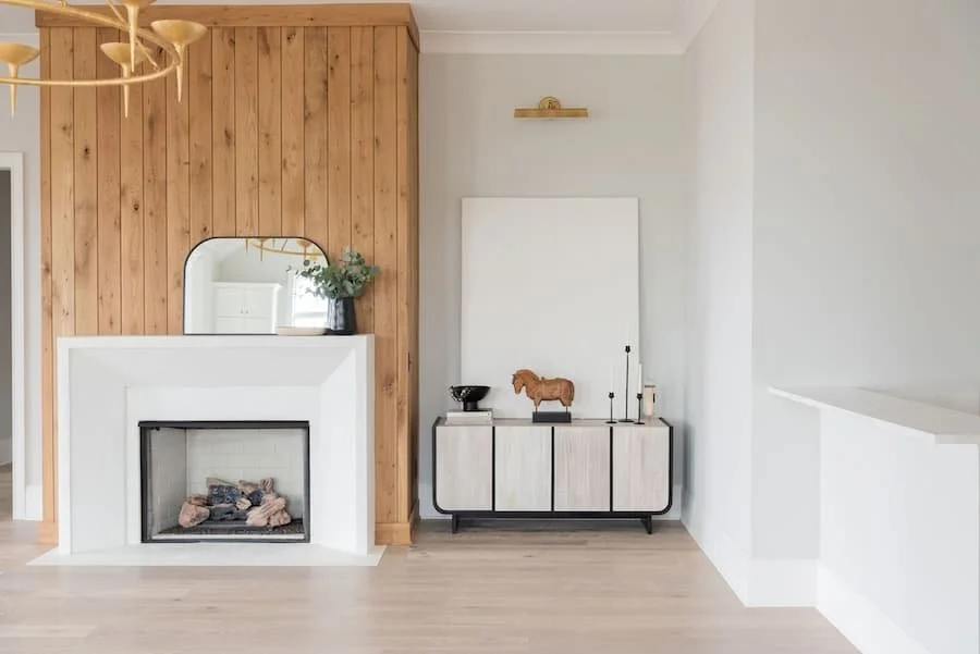 fireplace mantels / fireplace mantel ideas - white minimalist fireplace with warm wood surround and a mirror and vase of greenery on the mantel