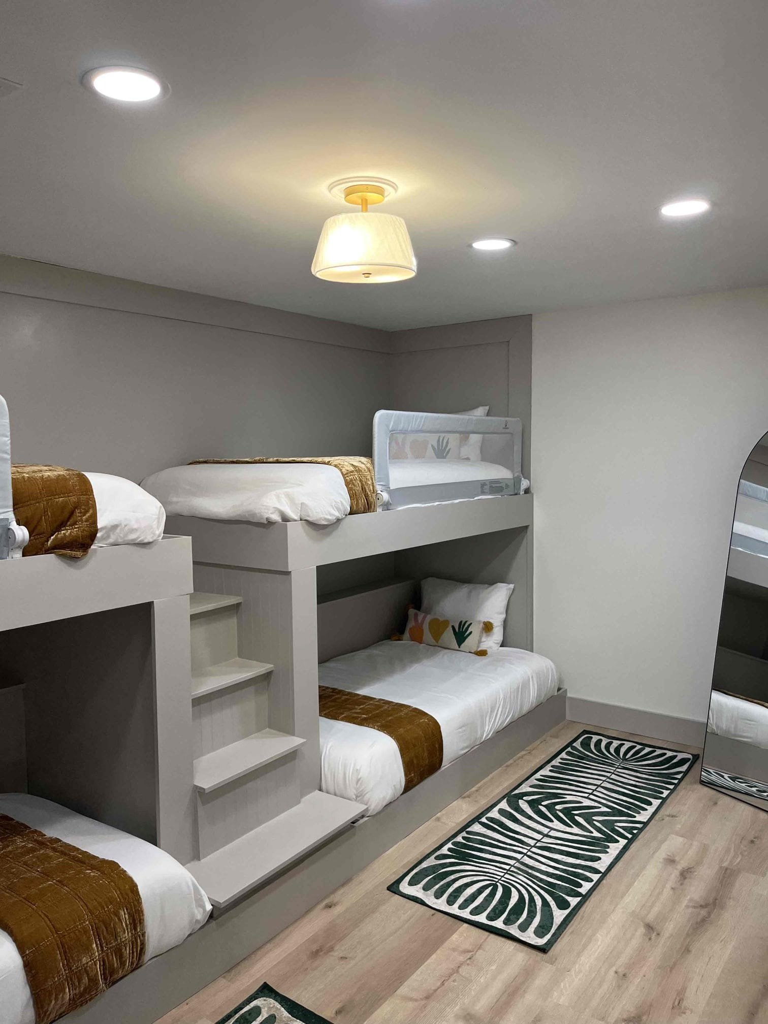 Custom-built bunk beds with integrated stairs in a finished basement bedroom, featuring modern lighting and neutral tones.