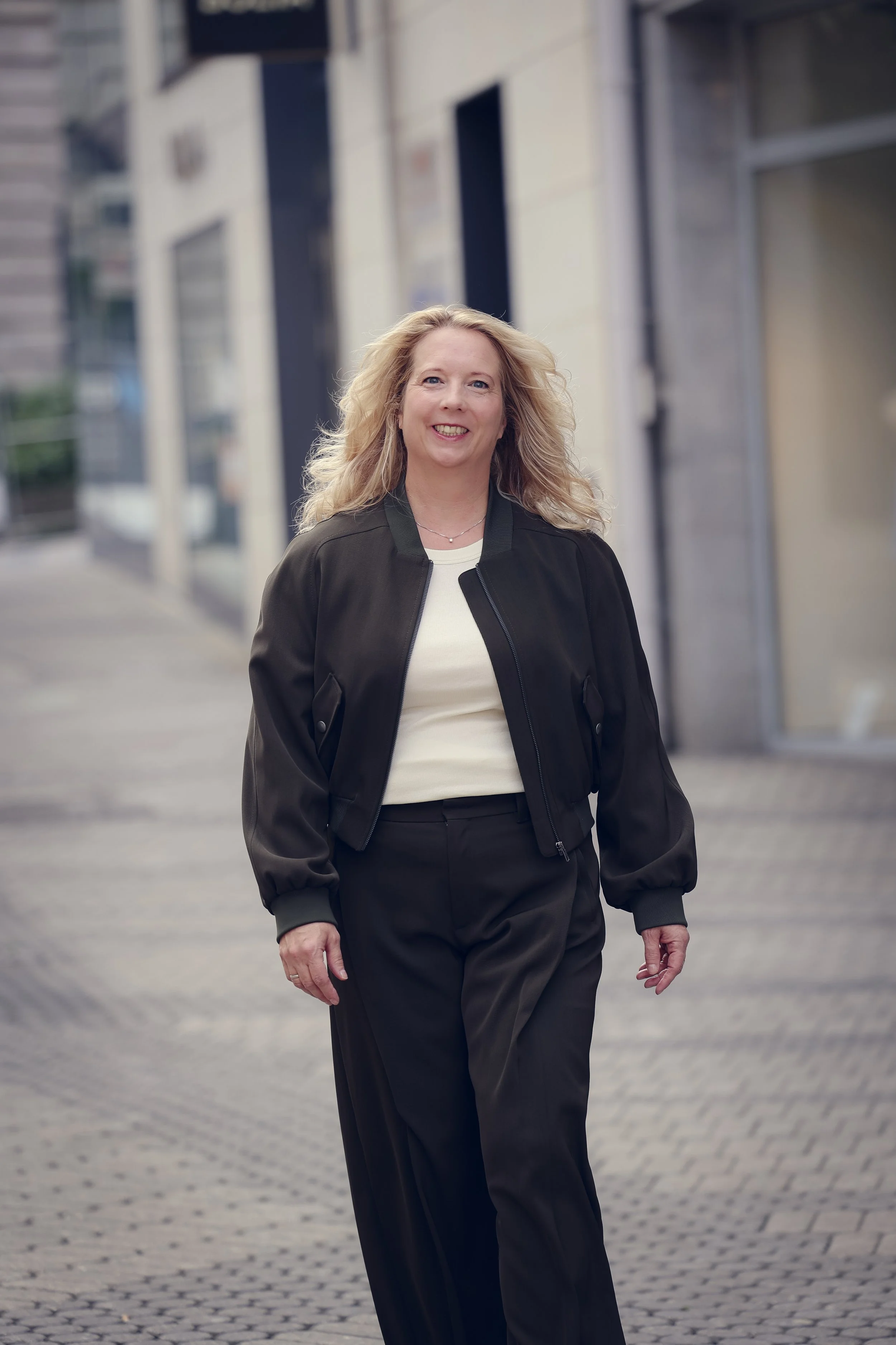 Die Gründerin von taxculture: eine lachende Frau in Business-Kleidung, spaziert auf einer Stadtstraße mit modernen Gebäuden im Hintergrund.