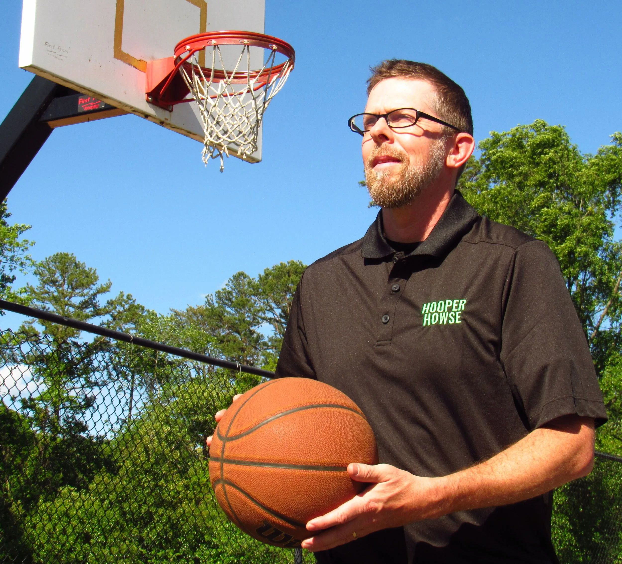 Man holding a basketball on an outdoor basketball court with a hoop and backboard.
