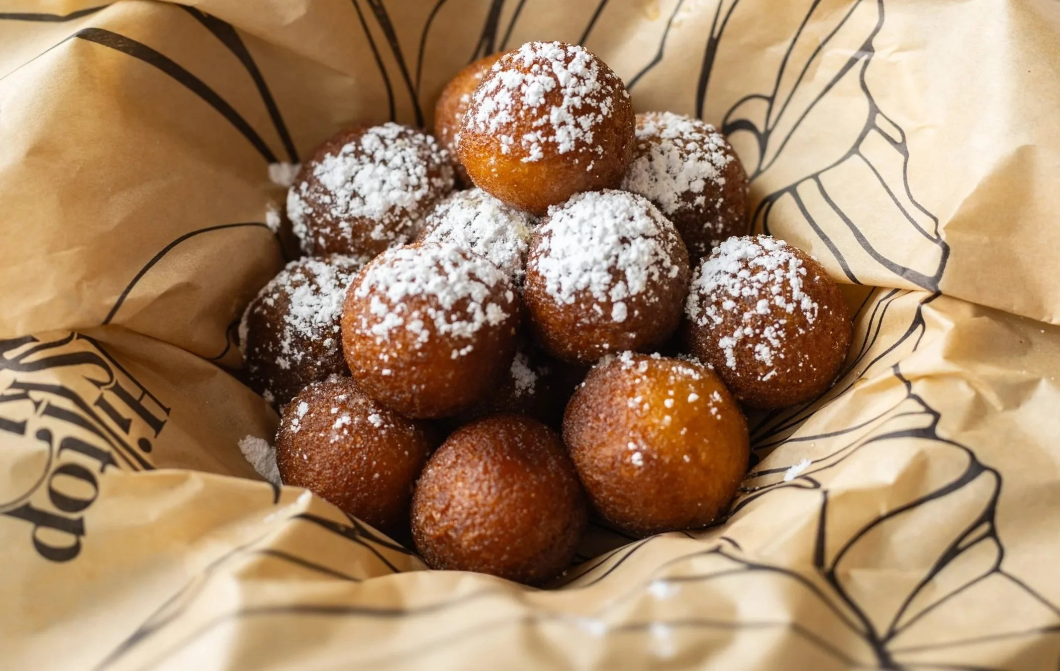 Close-up of deep-fried dough balls dusted with powdered sugar inside a paper-lined basket.