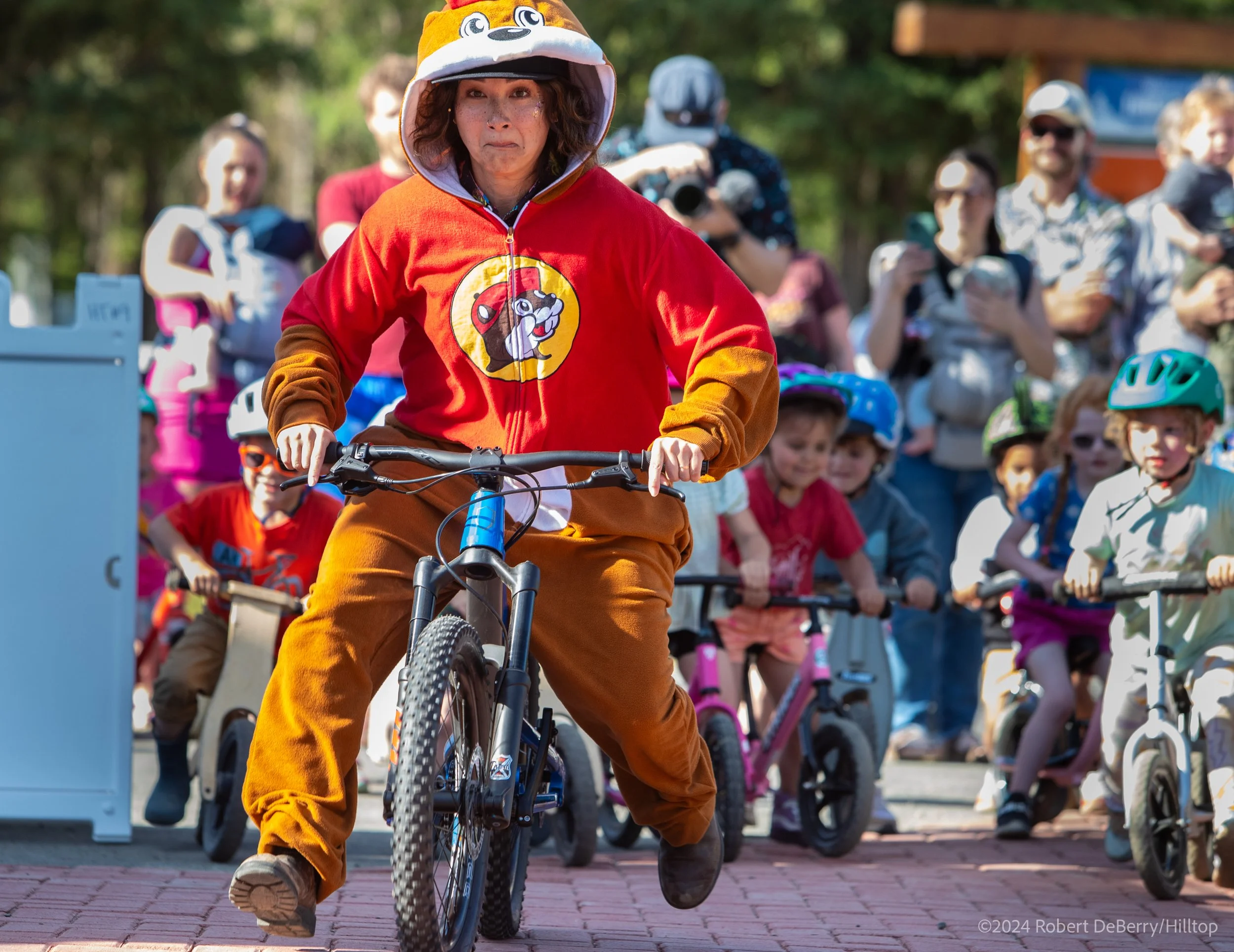 Woman wearing lion costume hoodie riding a bicycle during a parade, surrounded by spectators, some taking photos.
