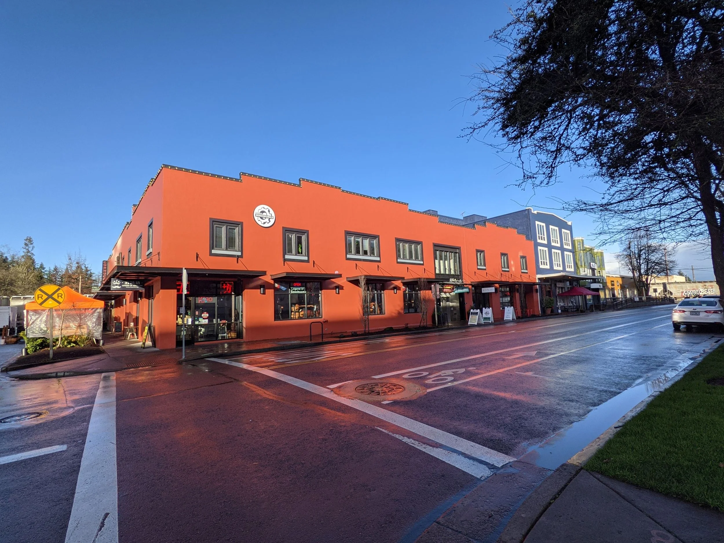 Colorful building on a wet street with reflections, trees, and a clear blue sky.