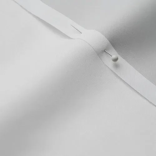 Close-up of white fabric with a pin and a pinhead holding the fabric in place.