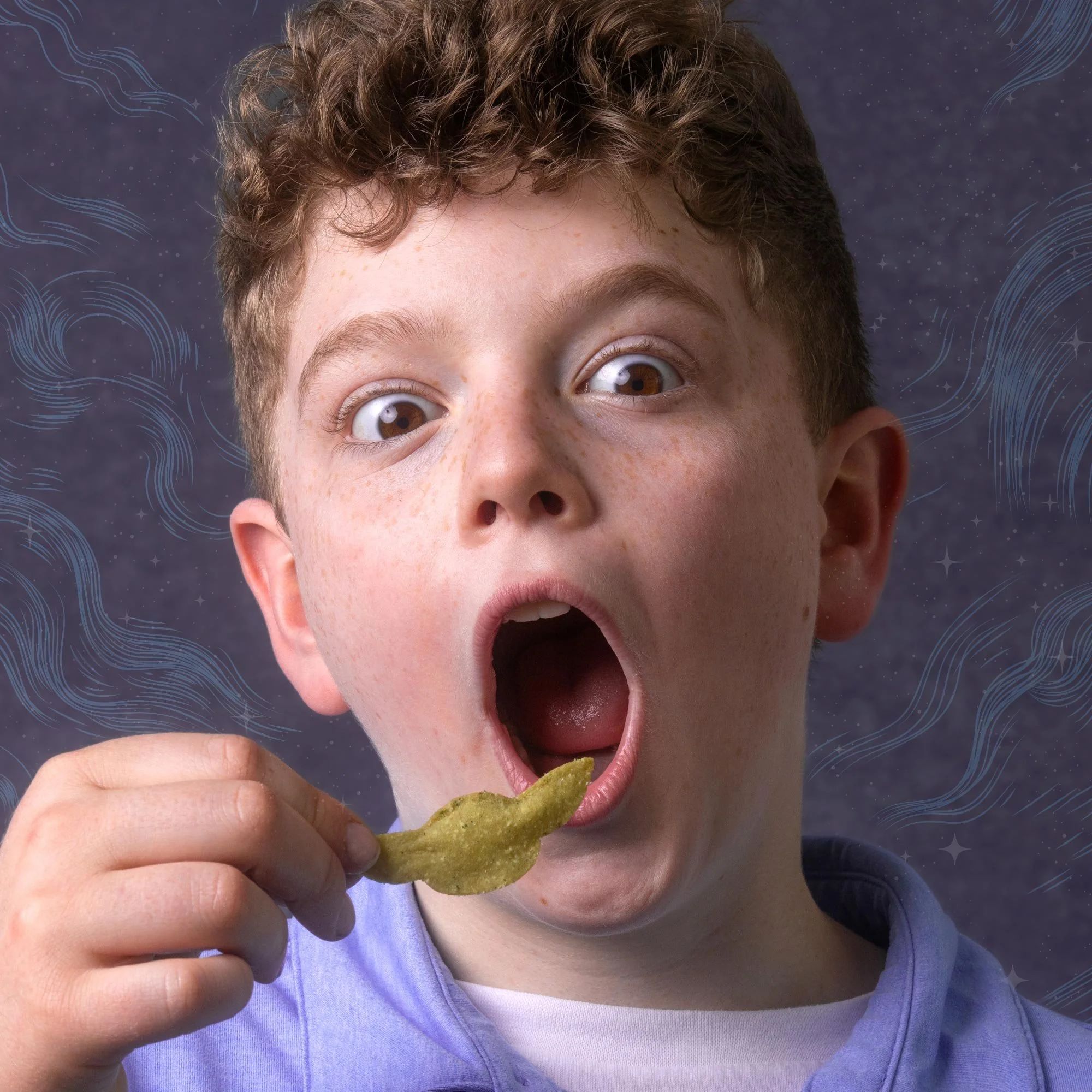 A young boy with curly brown hair and freckles is opening his mouth wide while holding a potato chip in his hand, about to eat it. He is wearing a purple jacket over a white shirt, with a dark background that has blue swirling patterns.