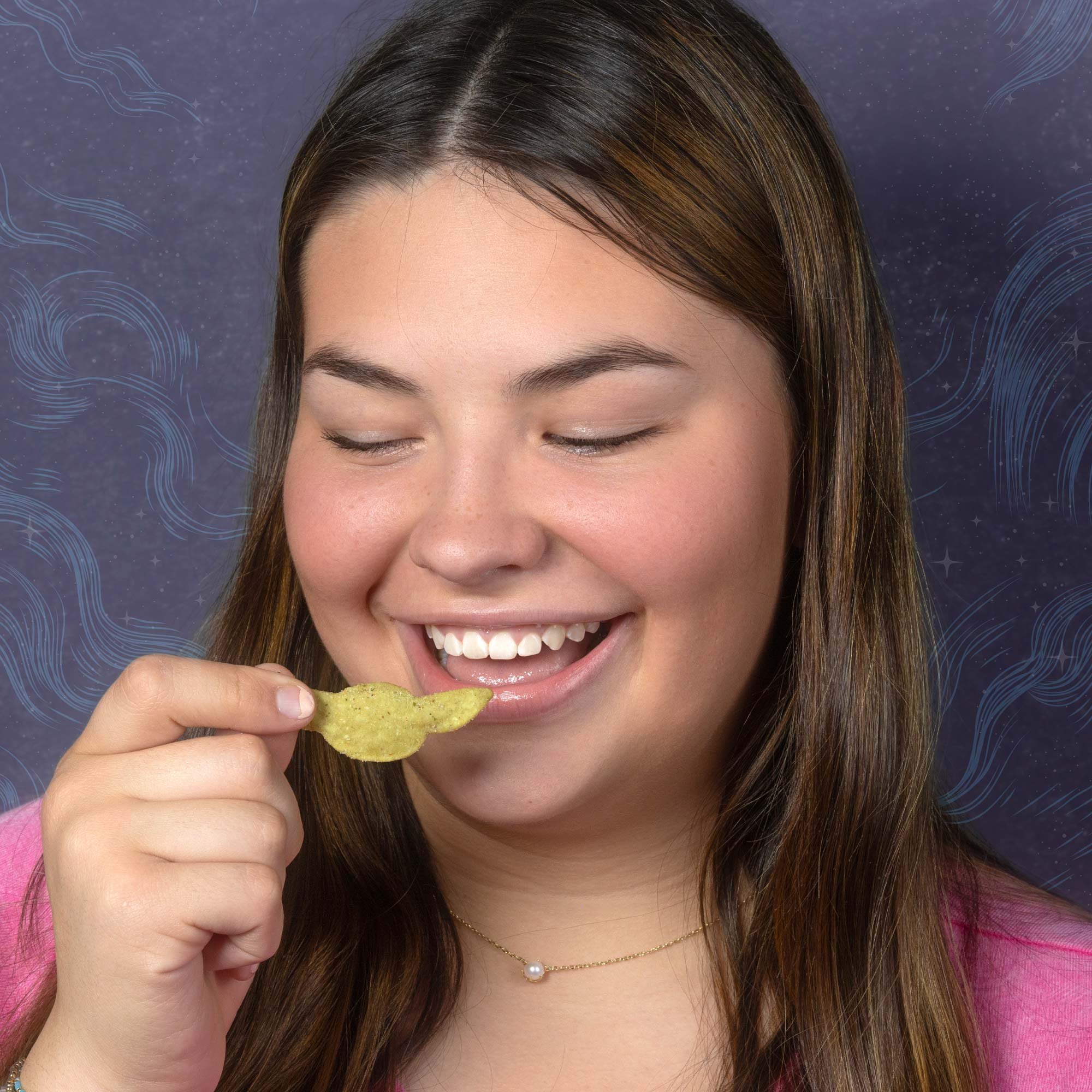 A woman with long brown hair smiling and holding a yellow potato chip near her mouth. She is wearing a pink top and a pearl necklace, with a dark, starry background with blue swirls.