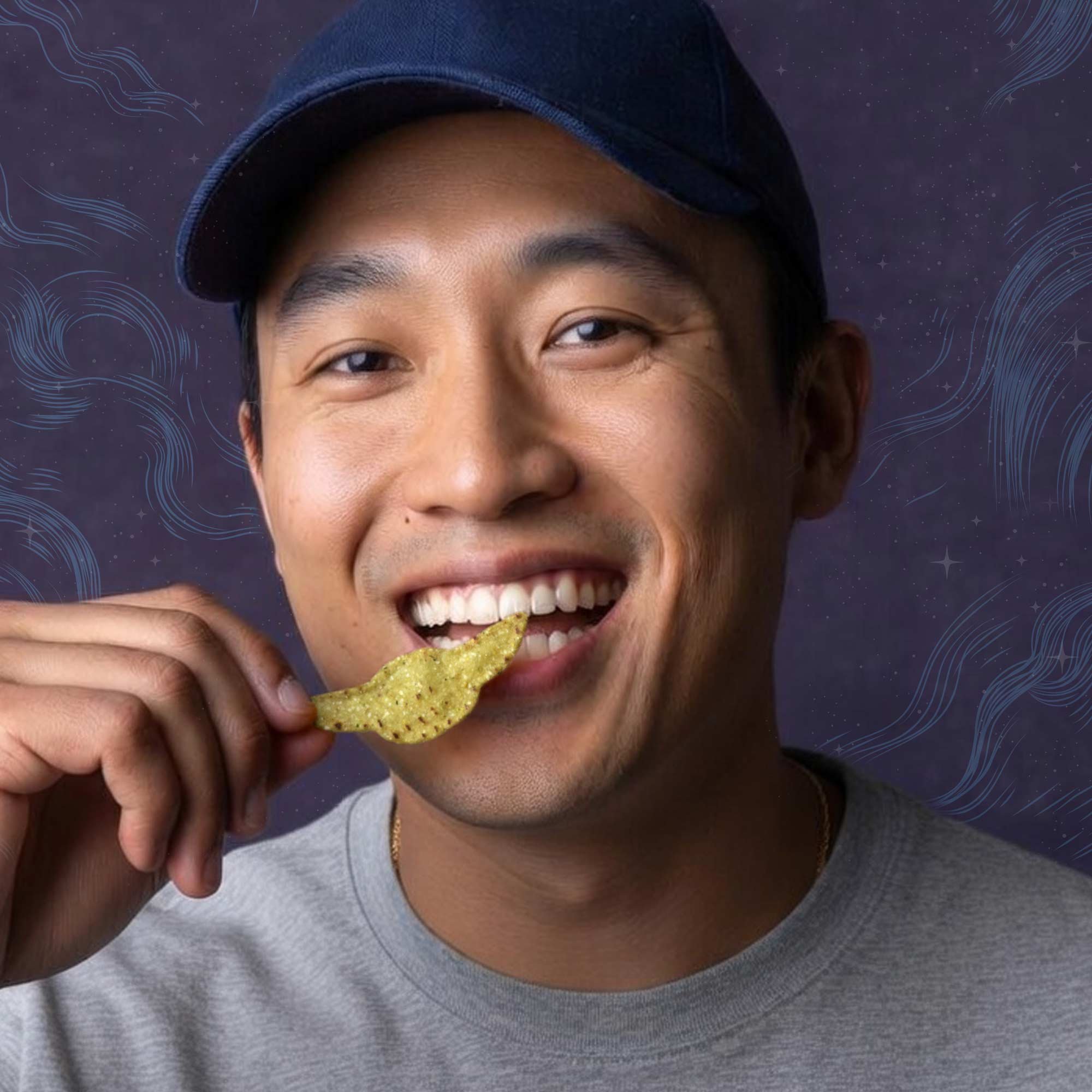 A man with tan skin wearing a gray shirt and a black cap, smiling and holding a potato chip near his mouth.