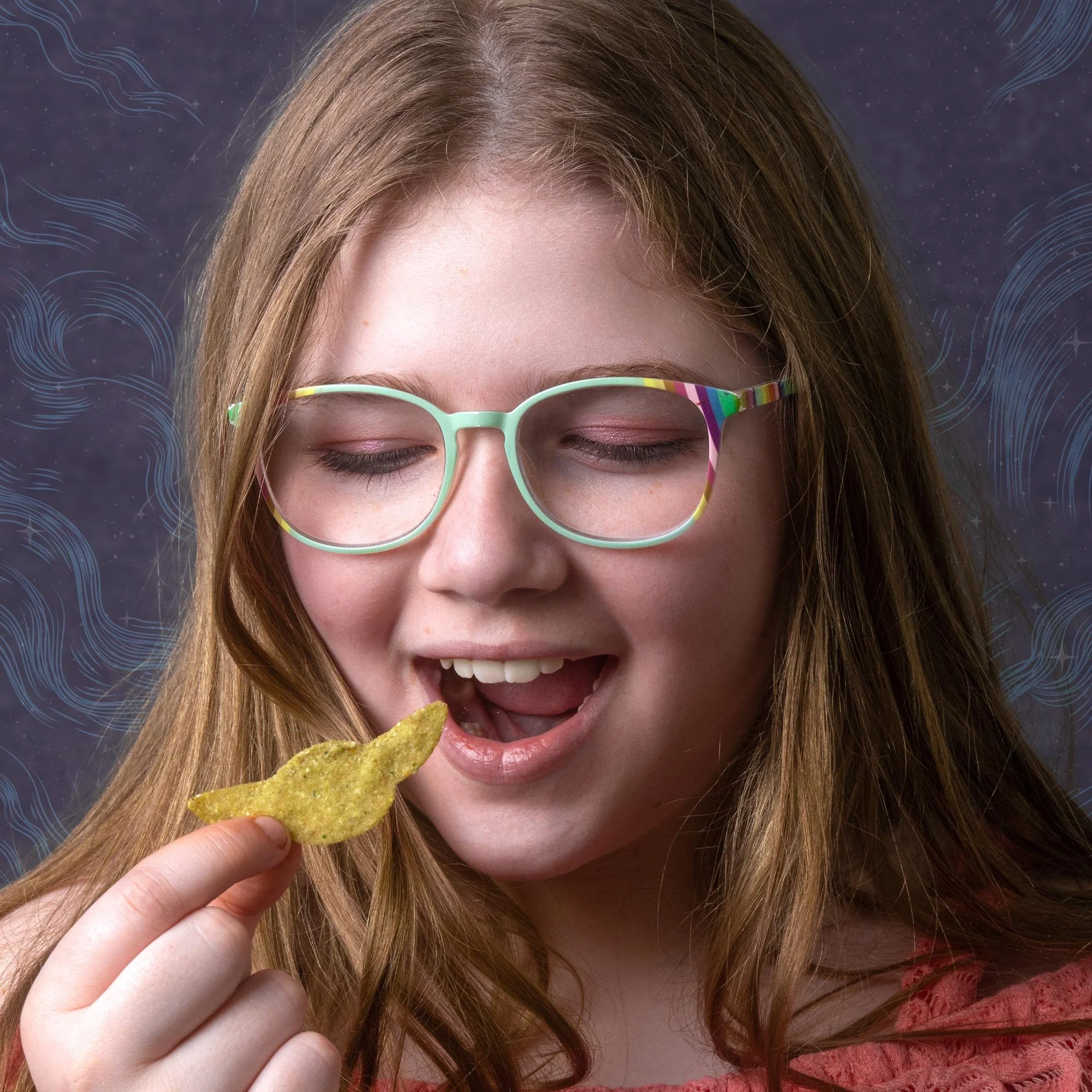 A girl with red hair wearing rainbow-colored glasses, smiling with eyes closed, holding a tortilla chip close to her mouth against a starry background with abstract blue lines.