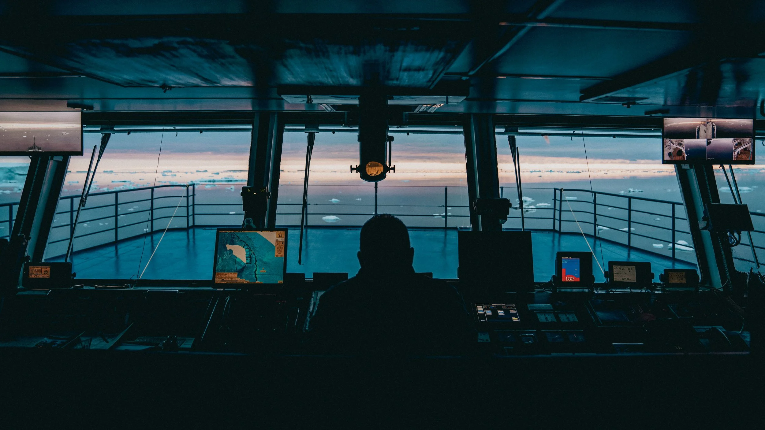 View from the cockpit of an airplane flying over clouds with a pilot in silhouette and digital displays in front.