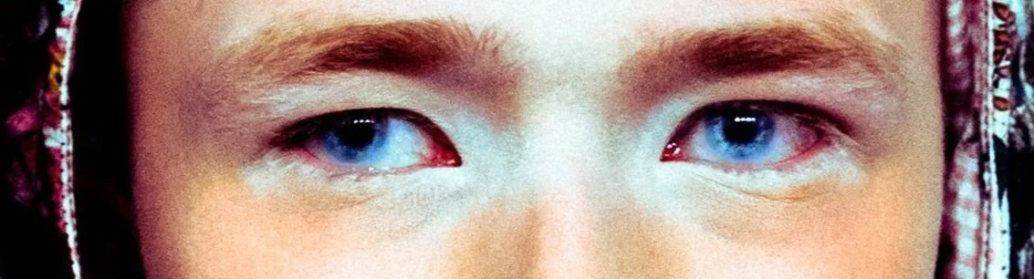 Close-up dos olhos de uma pessoa com olhos azuis, usando uma faixa colorida na cabeça.