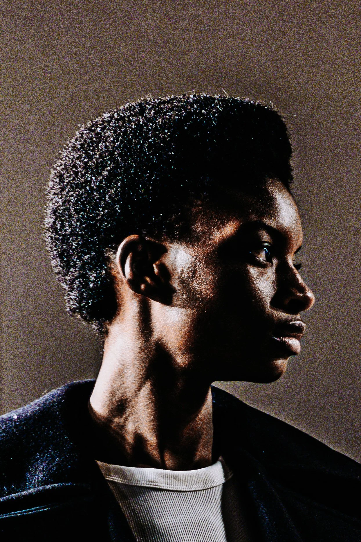Retrato de uma mulher afrodescendente com cabelo afro curto, usando uma jaqueta escura e uma camiseta branca, olhando para o lado.