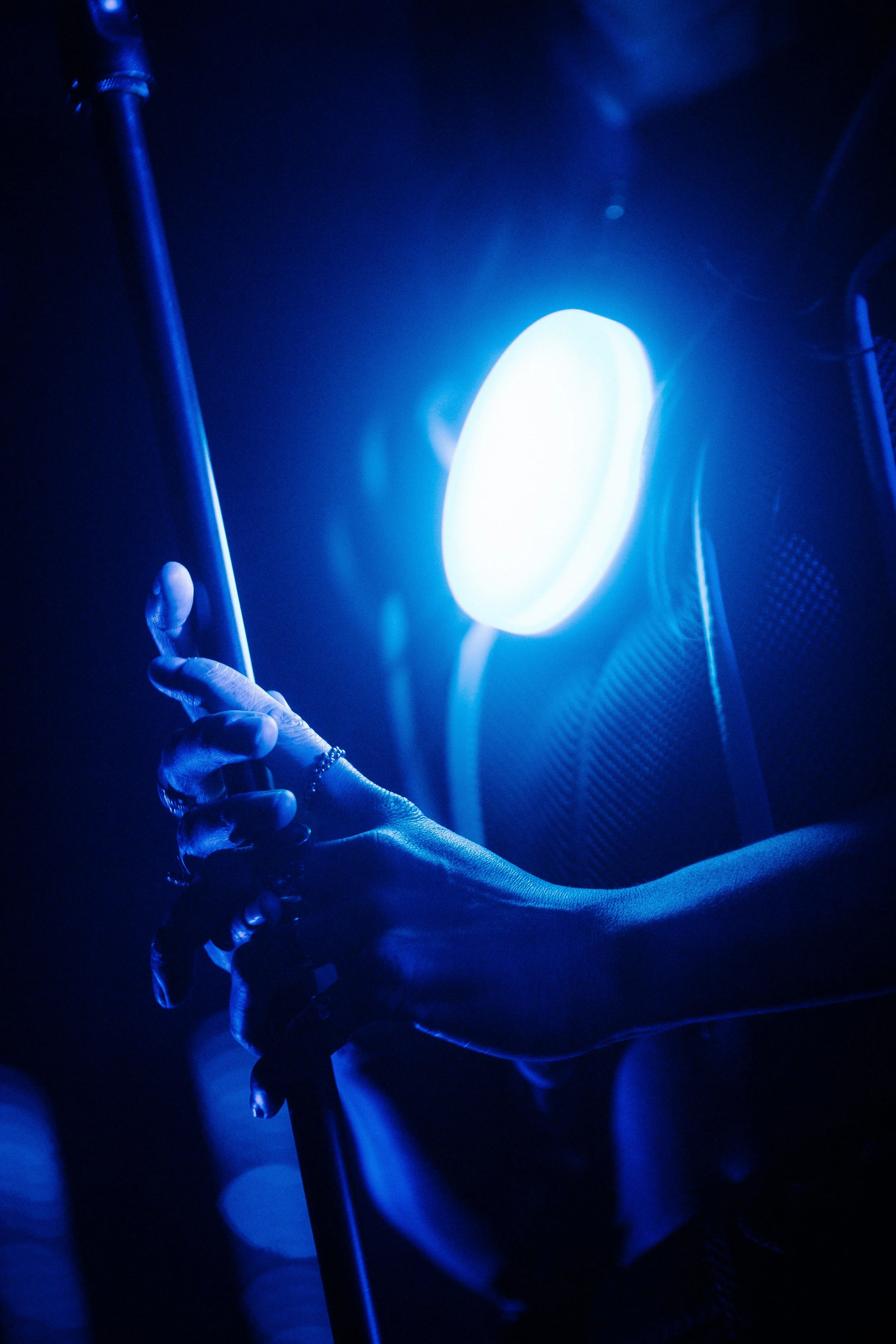 Mão de uma pessoa segurando uma bengala sob luz azul ao fundo, com iluminação escura e ambiente de baixa luz.