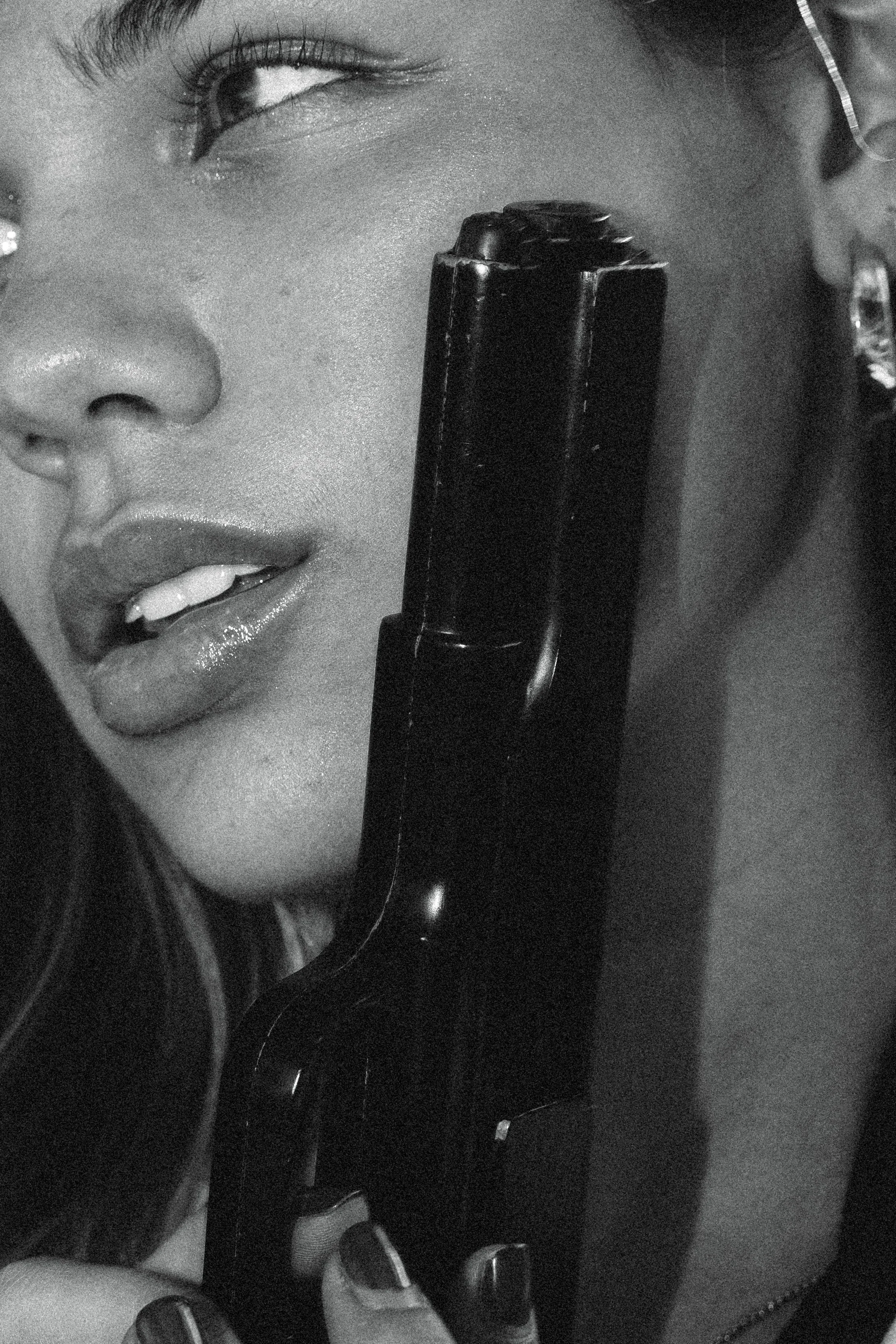 Close-up de uma mulher com cachos longos segurando um telefone antigo de discar estilo clássico preto, enquanto ela parece estar falando ou ouvindo. A imagem é em preto e branco, destaca o rosto, os lábios e o telefone.