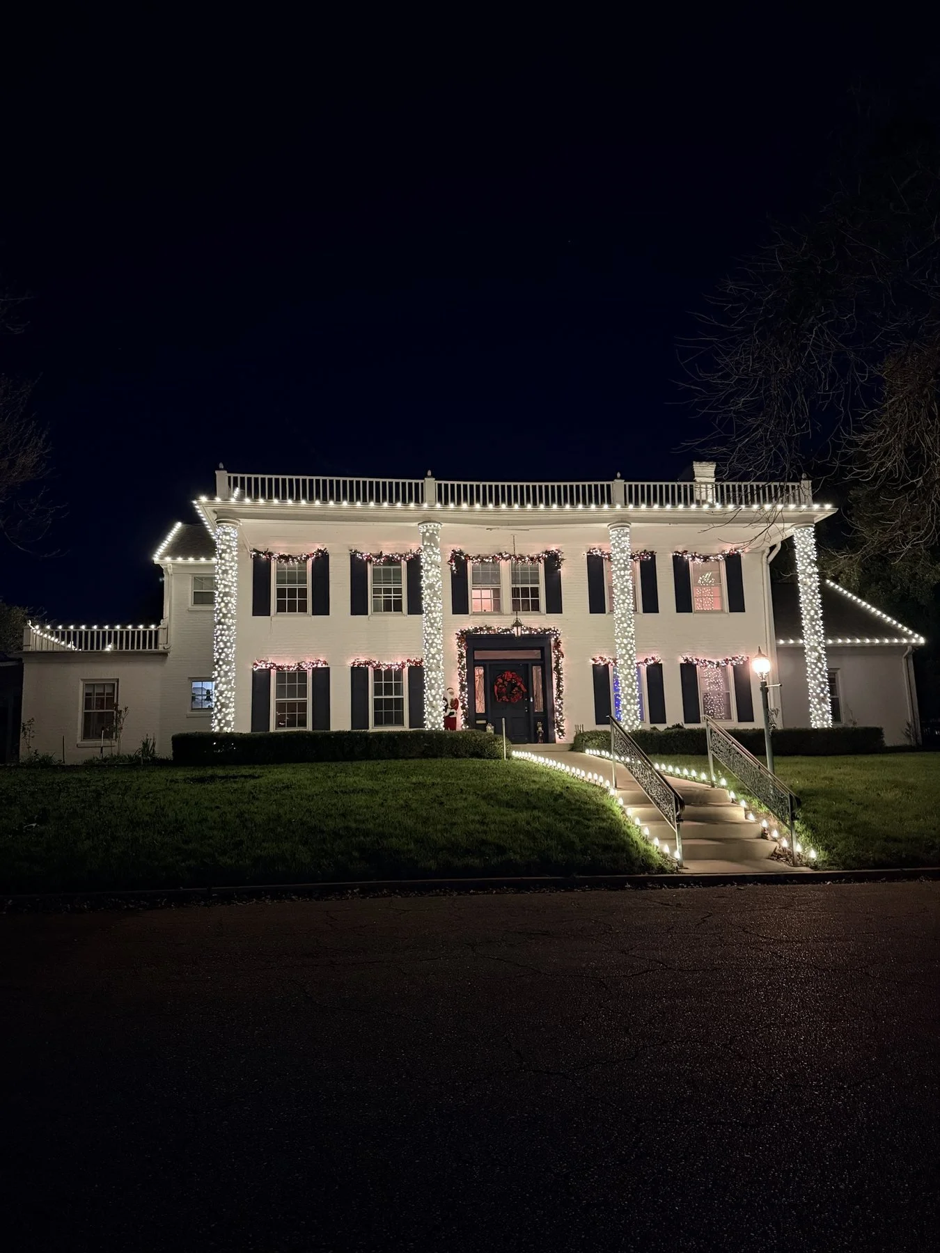 White two-story home with lit columns, garland above the windows and a lit roofline