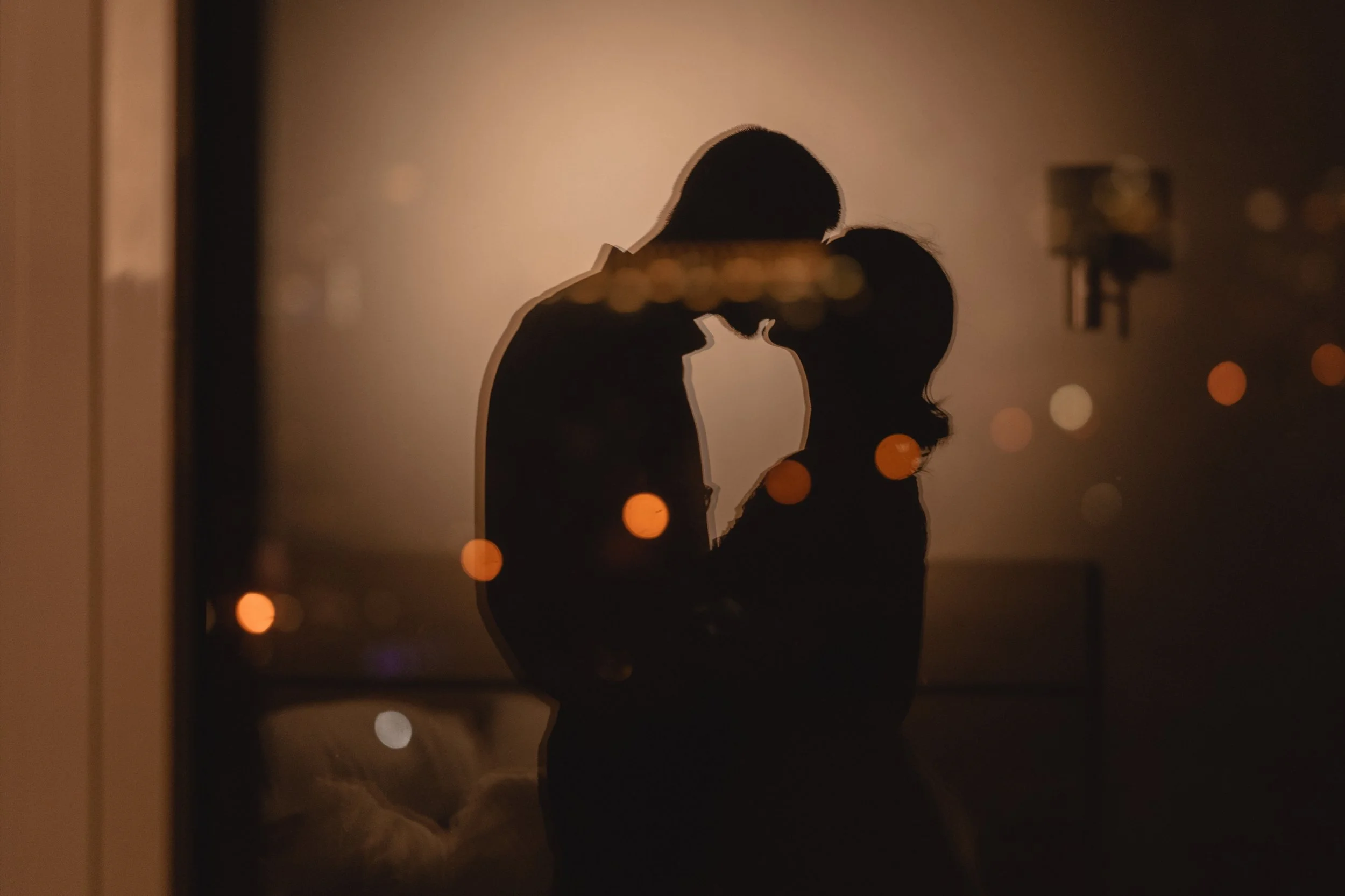 Silhouette of a couple leaning in for a kiss, with city lights blurred in the background at night.
