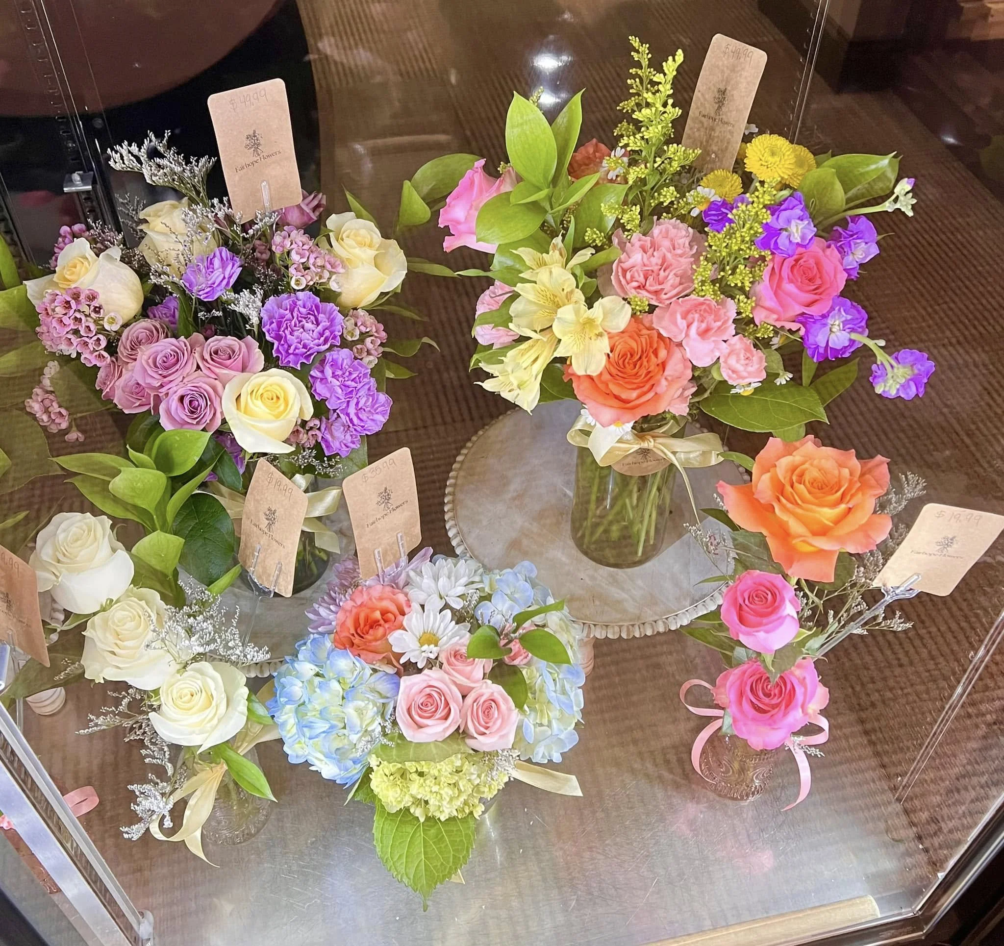 Various colorful flower bouquets displayed behind glass, featuring roses, lilies, hydrangeas, and other blooms.