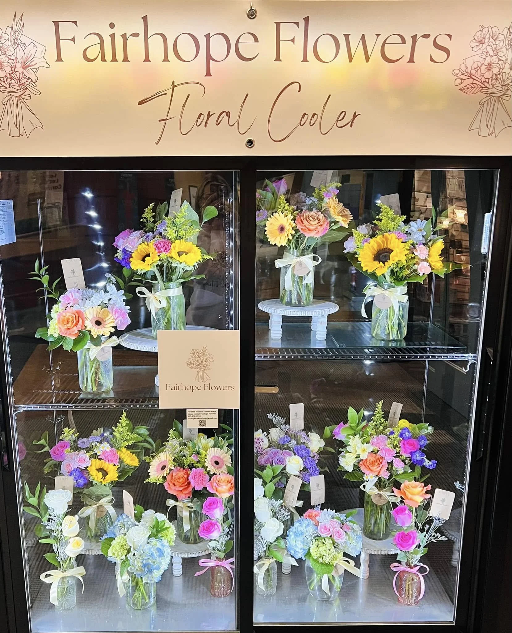 Display of colorful floral bouquets in glass vases inside a refrigerated showcase labeled "Fairhope Flowers Floral Cooler".